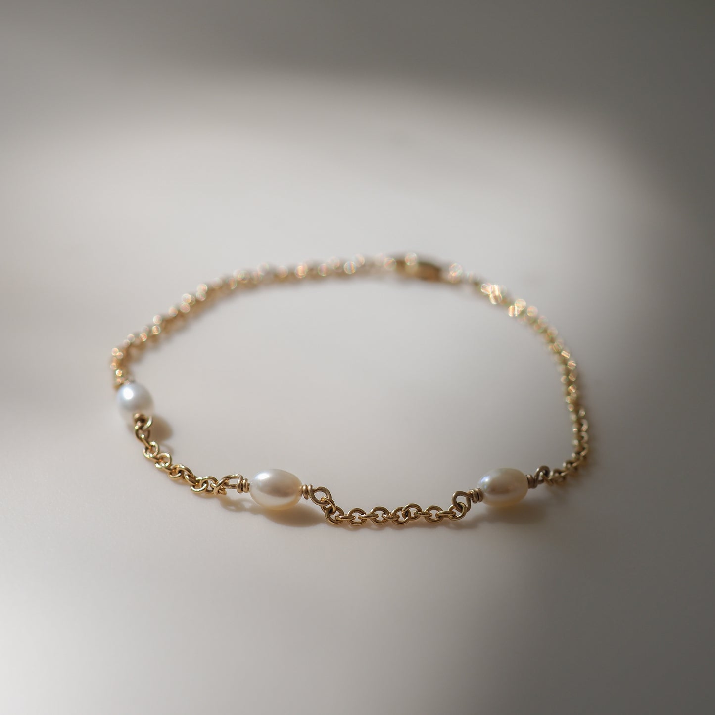Gold chain bracelet with spaced pearls, elegantly displayed on a neutral background, reflecting luxury and sophistication in jewellery design.