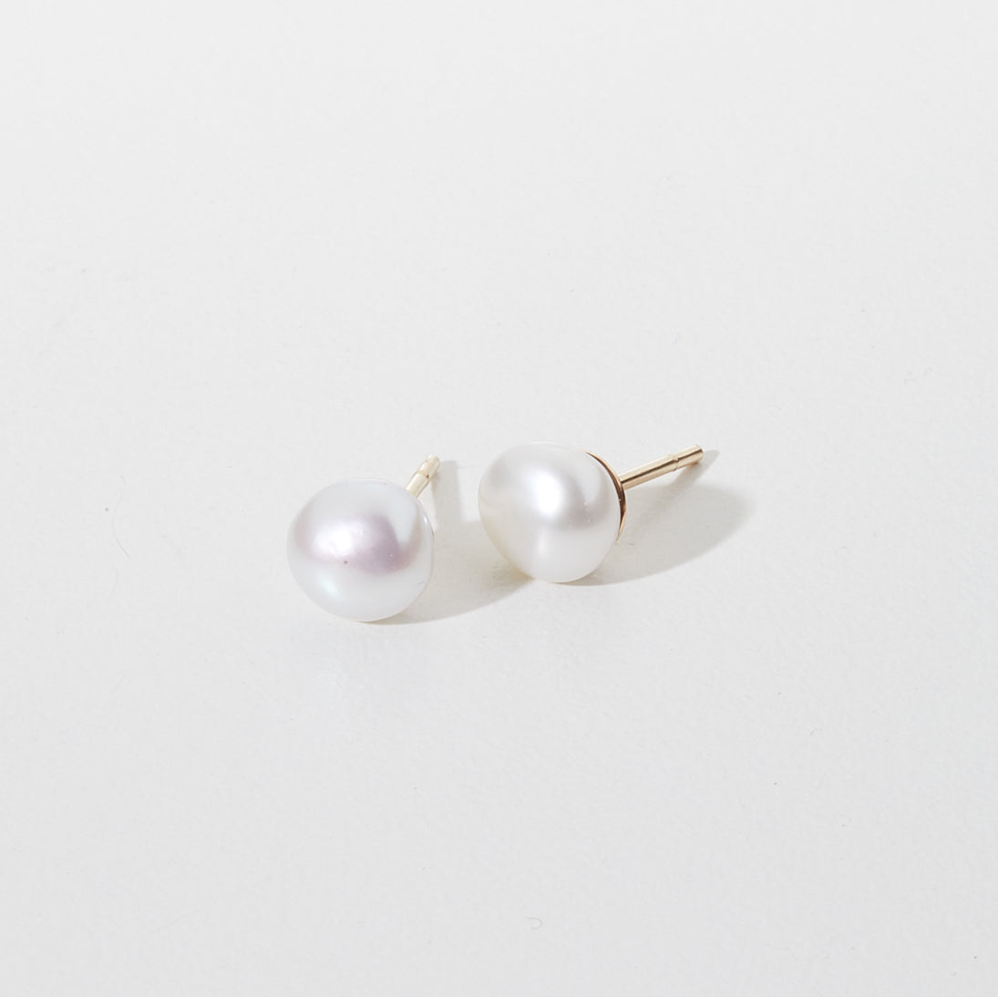 Pair of elegant white pearl stud earrings with gold posts on a plain background. Perfect for luxury jewellery lovers seeking timeless style.