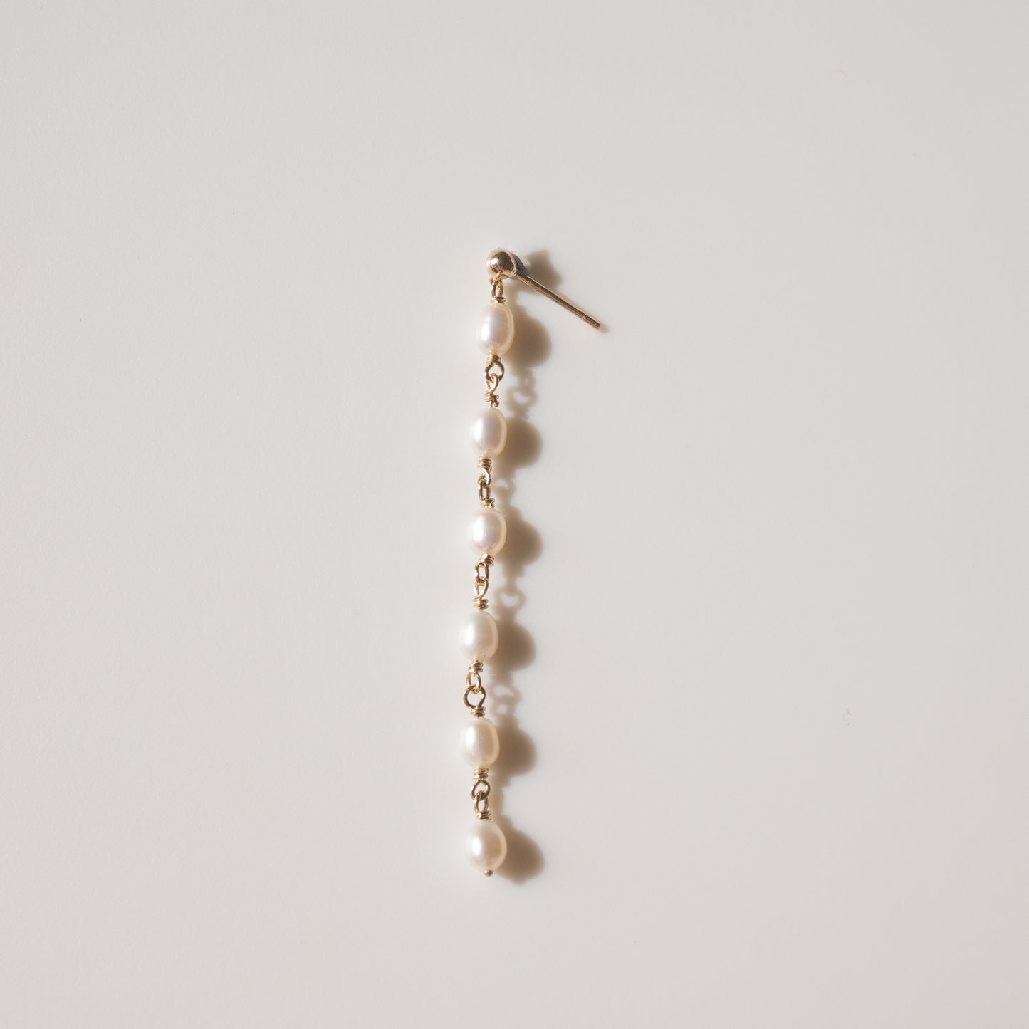 Elegant gold earring with seven lustrous pearls on a white background, showcasing luxury jewellery design.