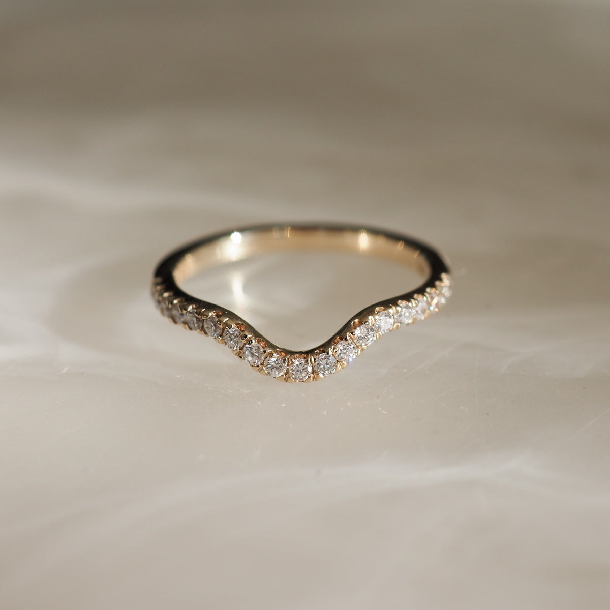 Elegant gold ring with wavy design, adorned with sparkling diamonds. Luxurious jewellery piece on a soft, light-toned background.