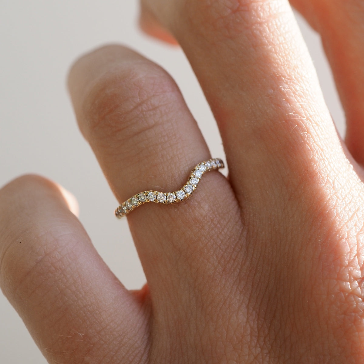 Elegant wave-shaped diamond ring on a finger, featuring a gold band adorned with sparkling diamonds, epitomising luxury jewellery style.
