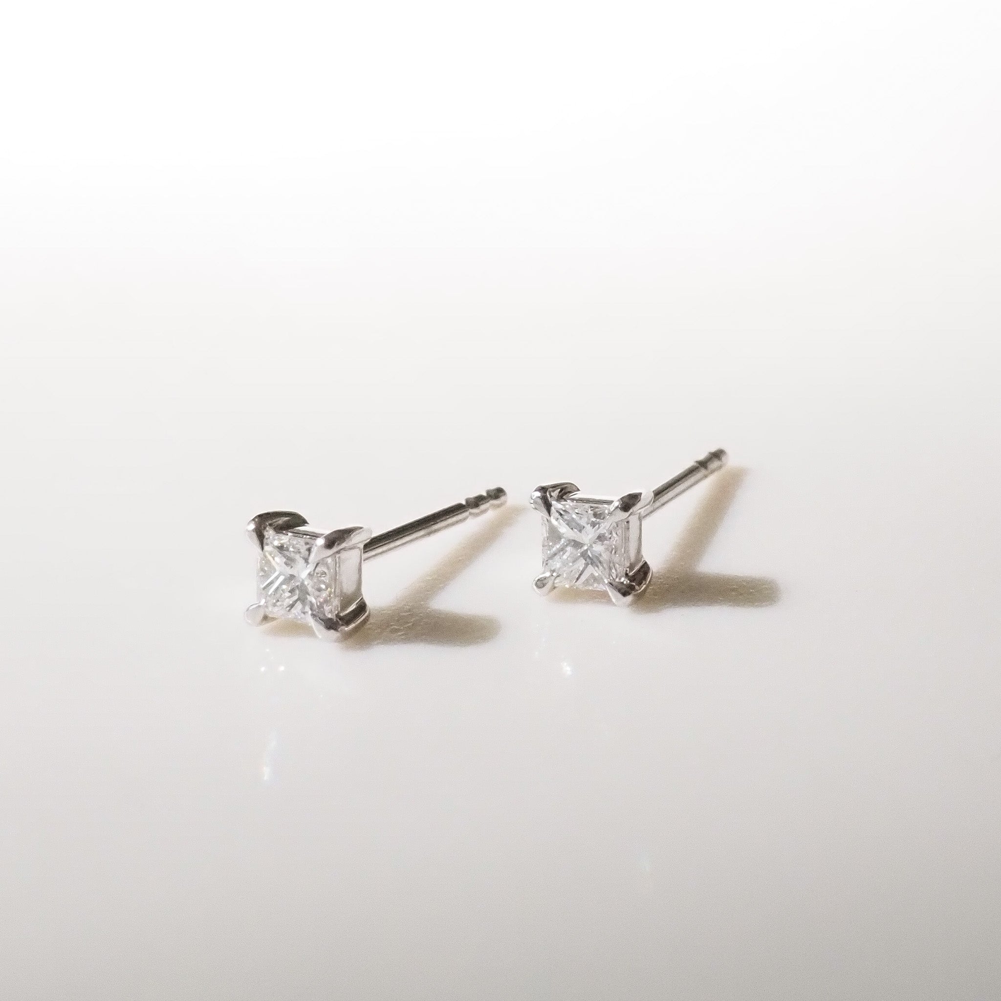 Pair of princess diamond stud earrings on a light gray background