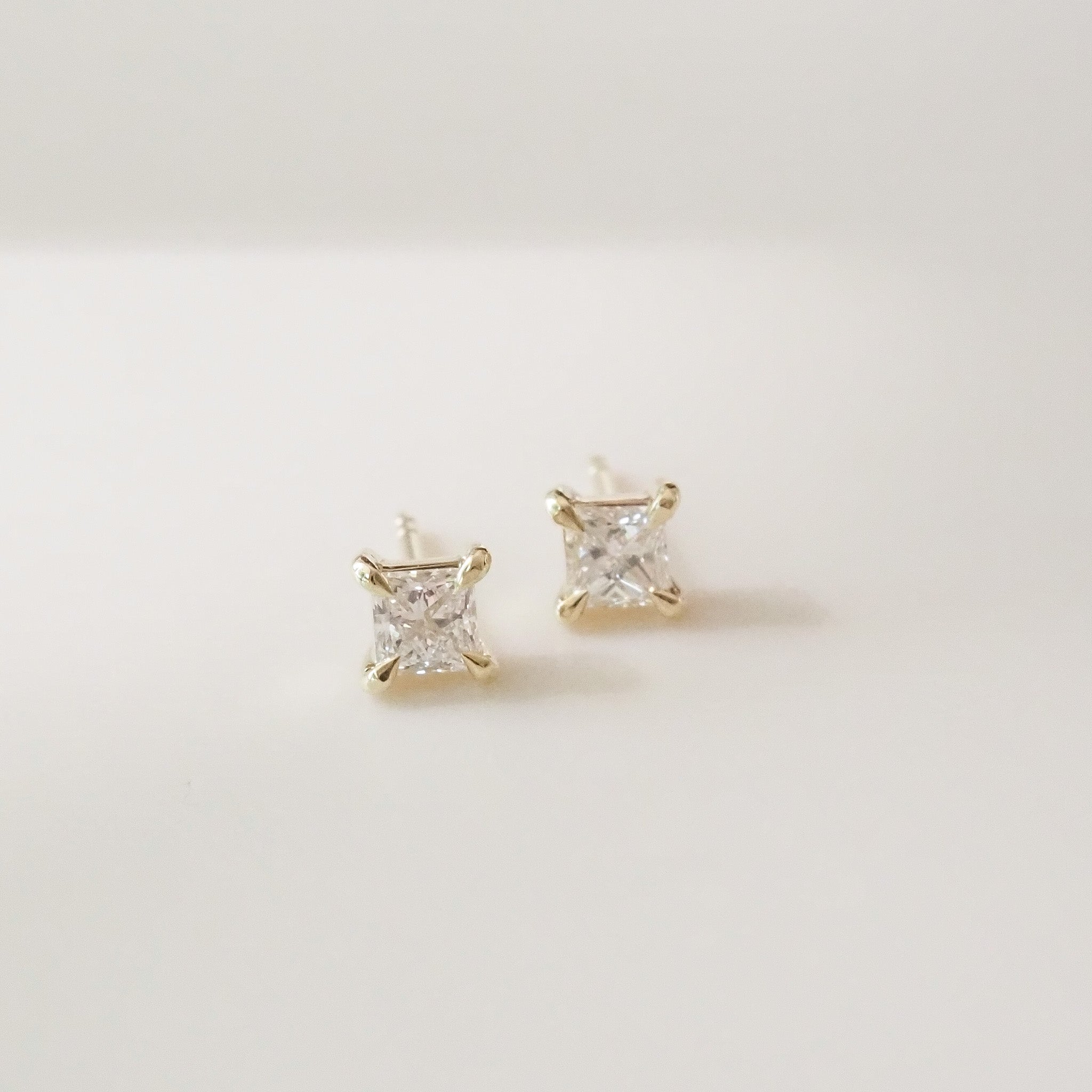 Gold princess earrings with clear gemstones on a light gray background