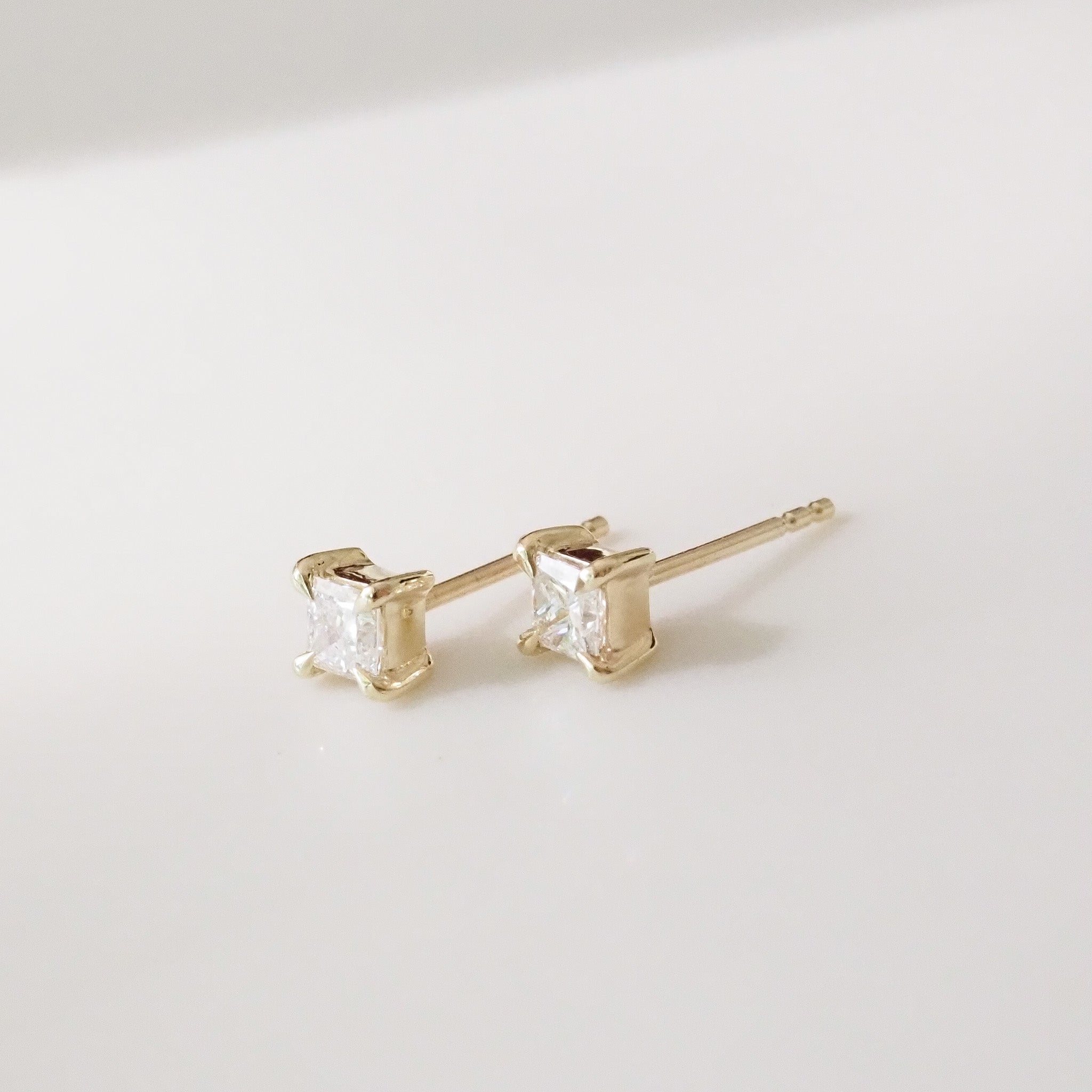 Gold princess earrings with clear gemstones on a light gray background