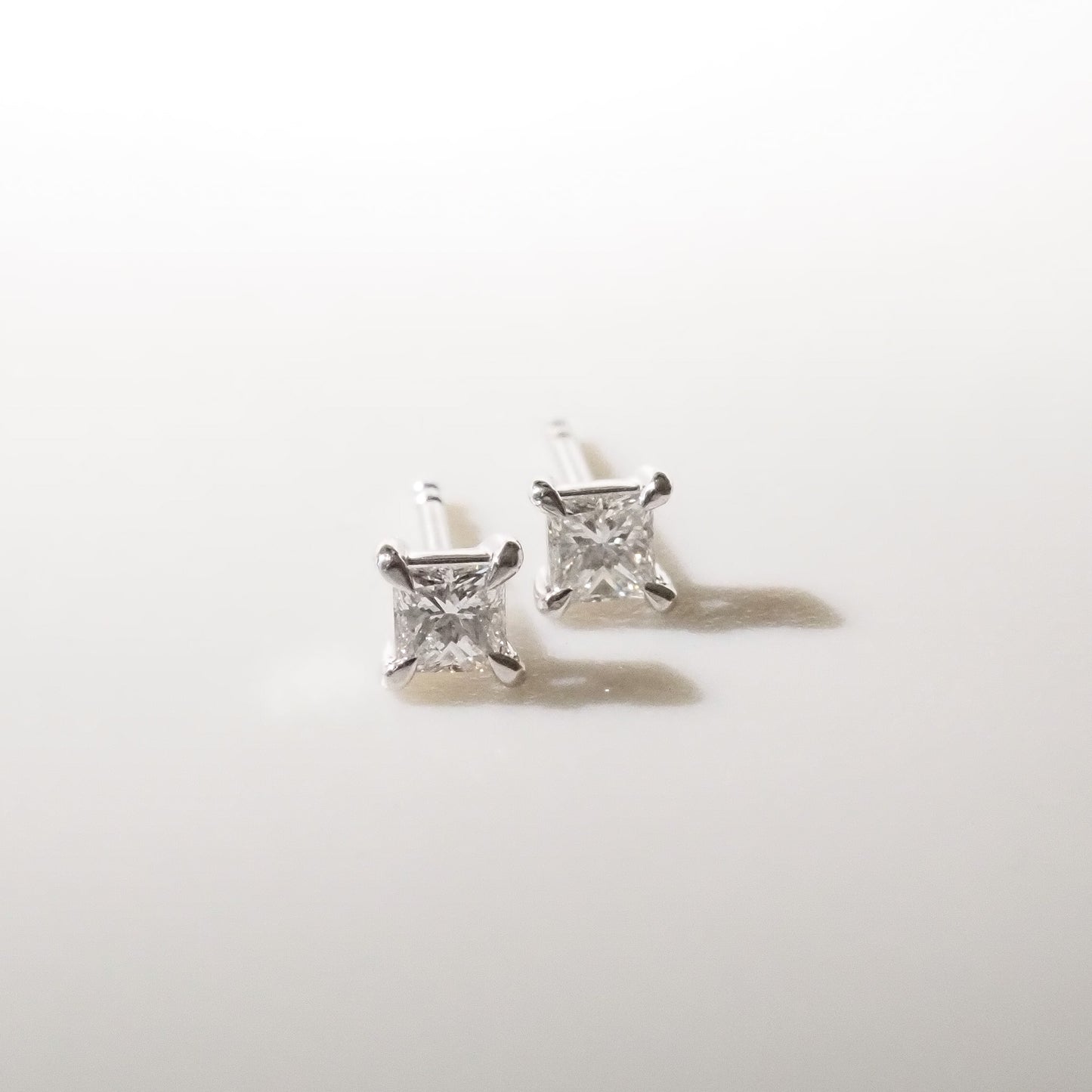 Pair of princess diamond stud earrings on a light gray background