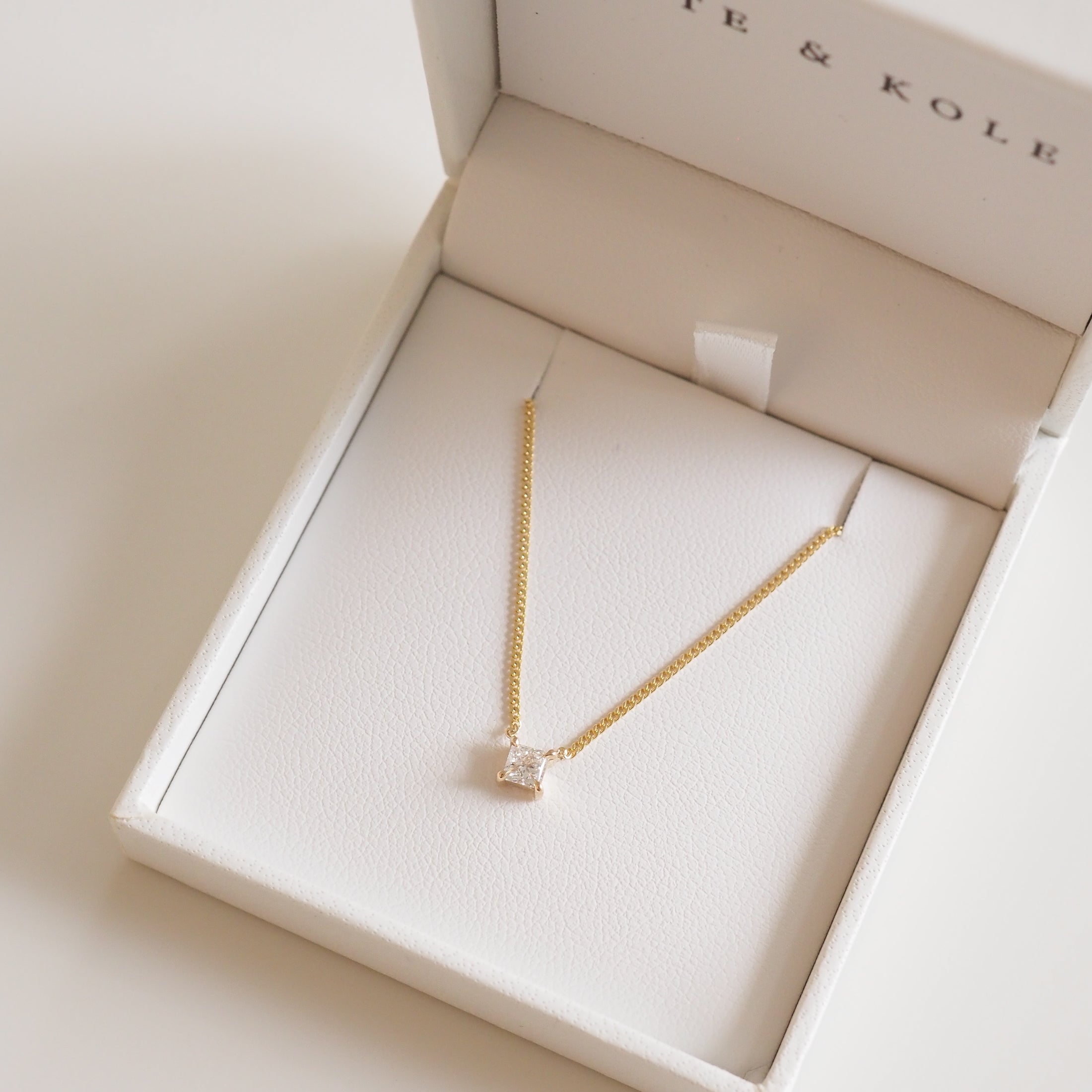 Gold necklace with square pendant in an open white jewellery box, featuring elegant and minimalist design, perfect for luxury accessorising.