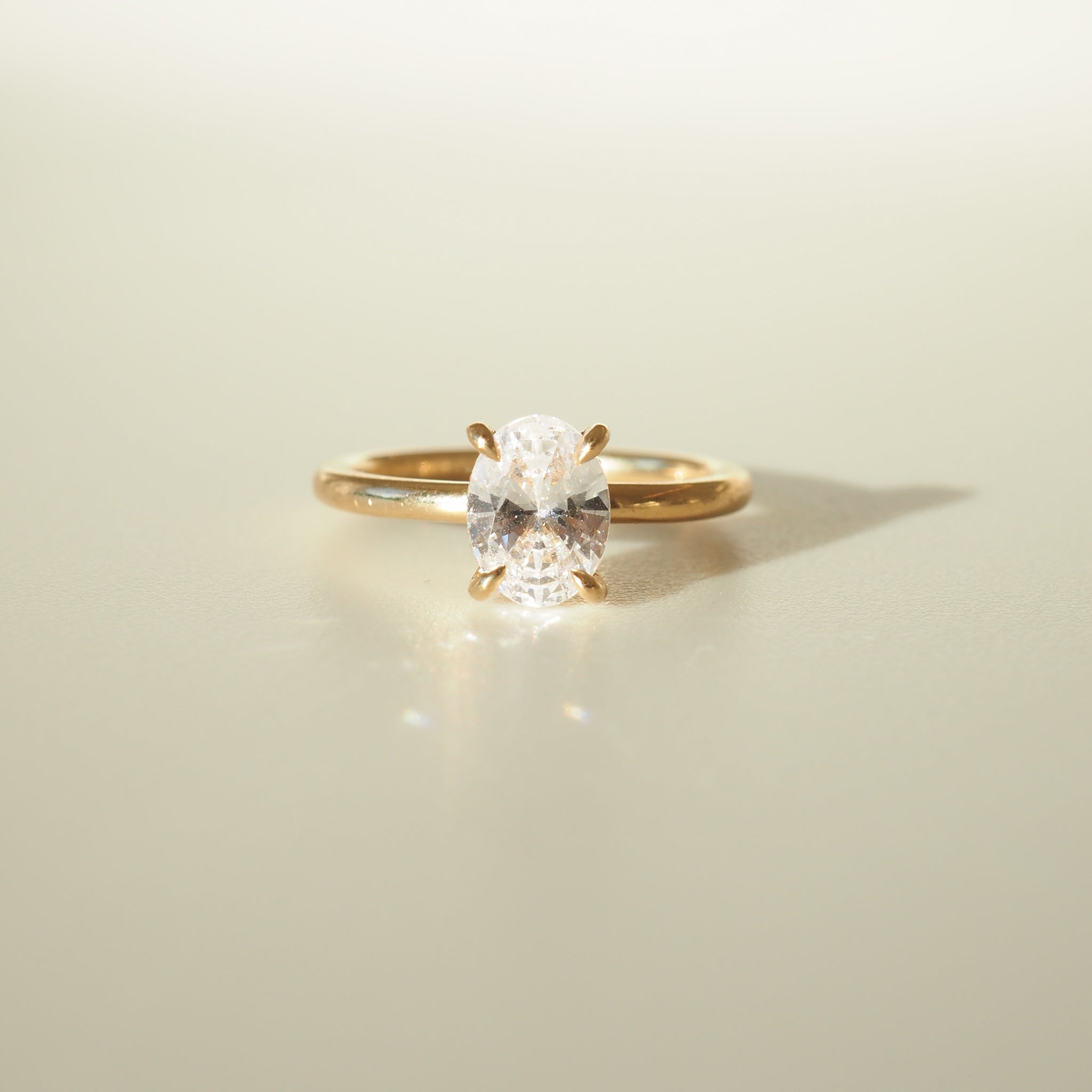 Gold ring with an oval-cut diamond solitaire, elegantly displayed on a soft, light background. Perfect for luxury jewellery lovers.
