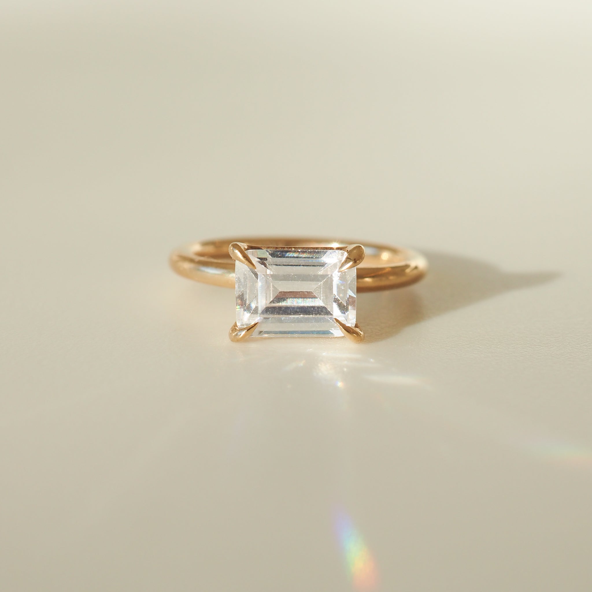 Emerald-cut diamond ring with a gold band, elegantly displayed on a soft light background, showcasing luxurious jewellery craftsmanship.