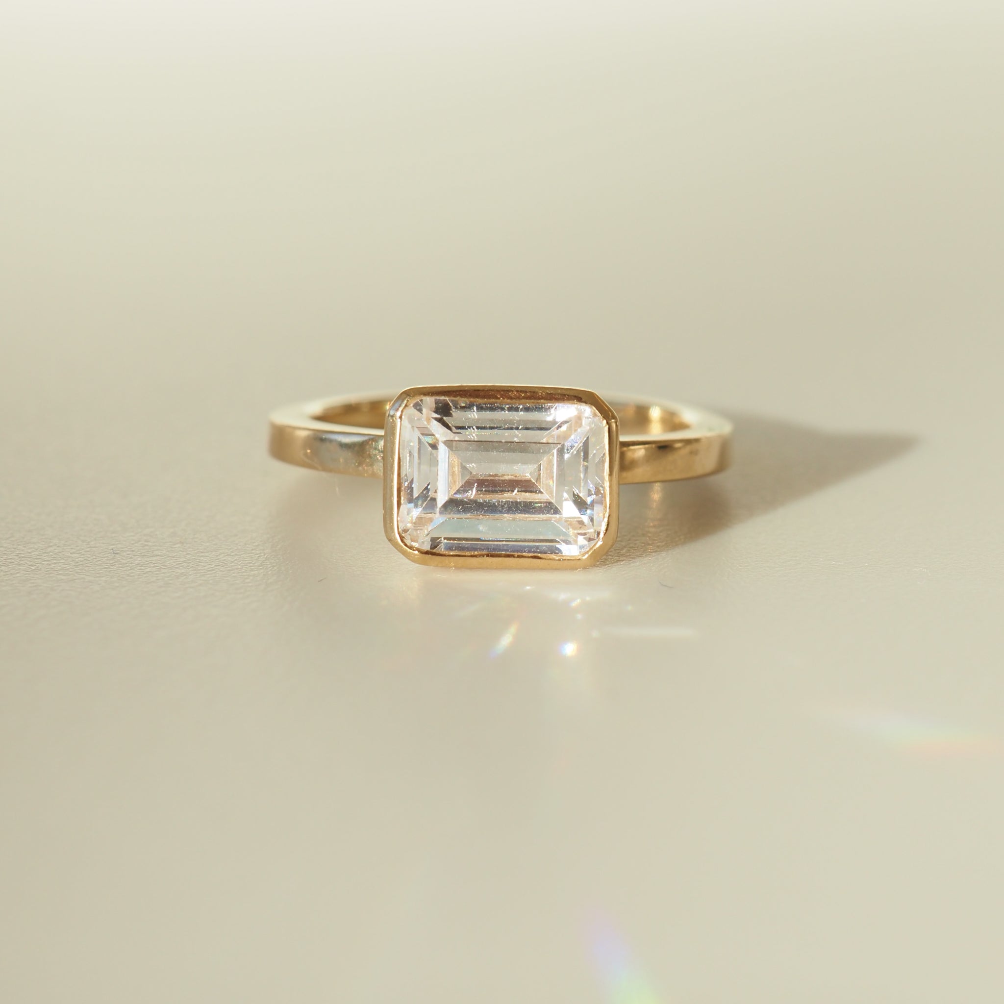 Emerald-cut diamond ring in a gold band, elegantly displayed on a soft beige background. Perfect for luxury jewellery enthusiasts.