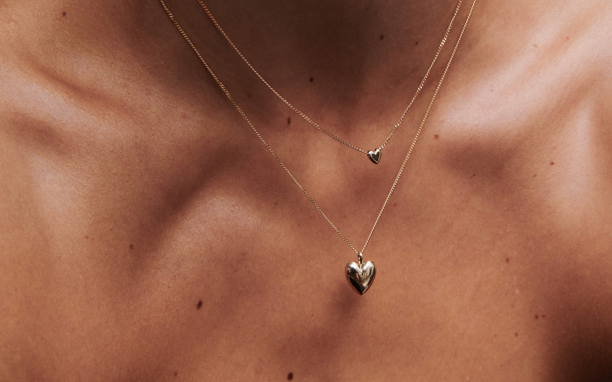 Close-up of layered gold heart necklaces on a woman’s décolletage – minimalist fine jewellery by Kate & Kole