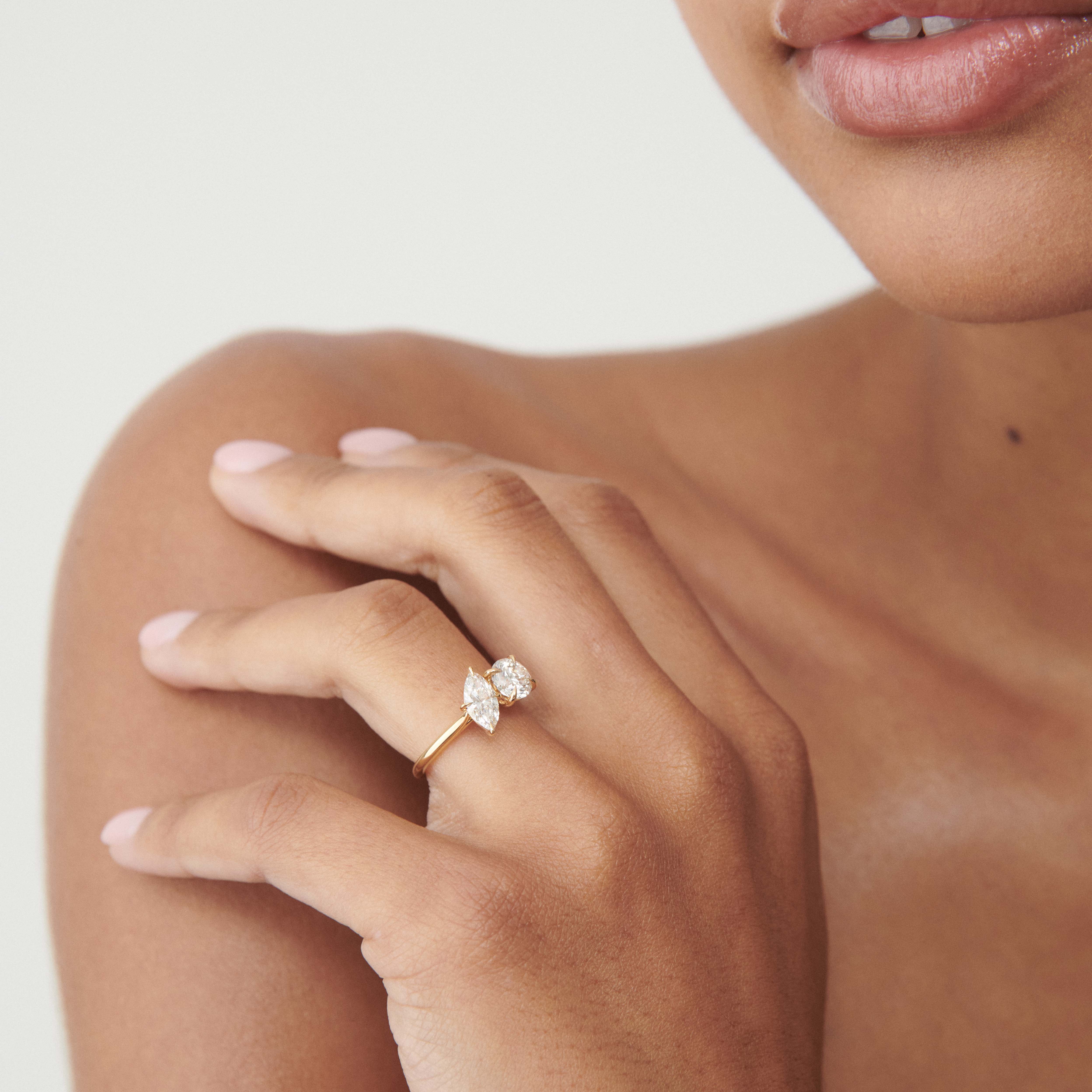 Woman's hand with a two-stone, gold engagement ring featuring large diamonds. Focus on luxury, elegance, and fine jewellery detail.