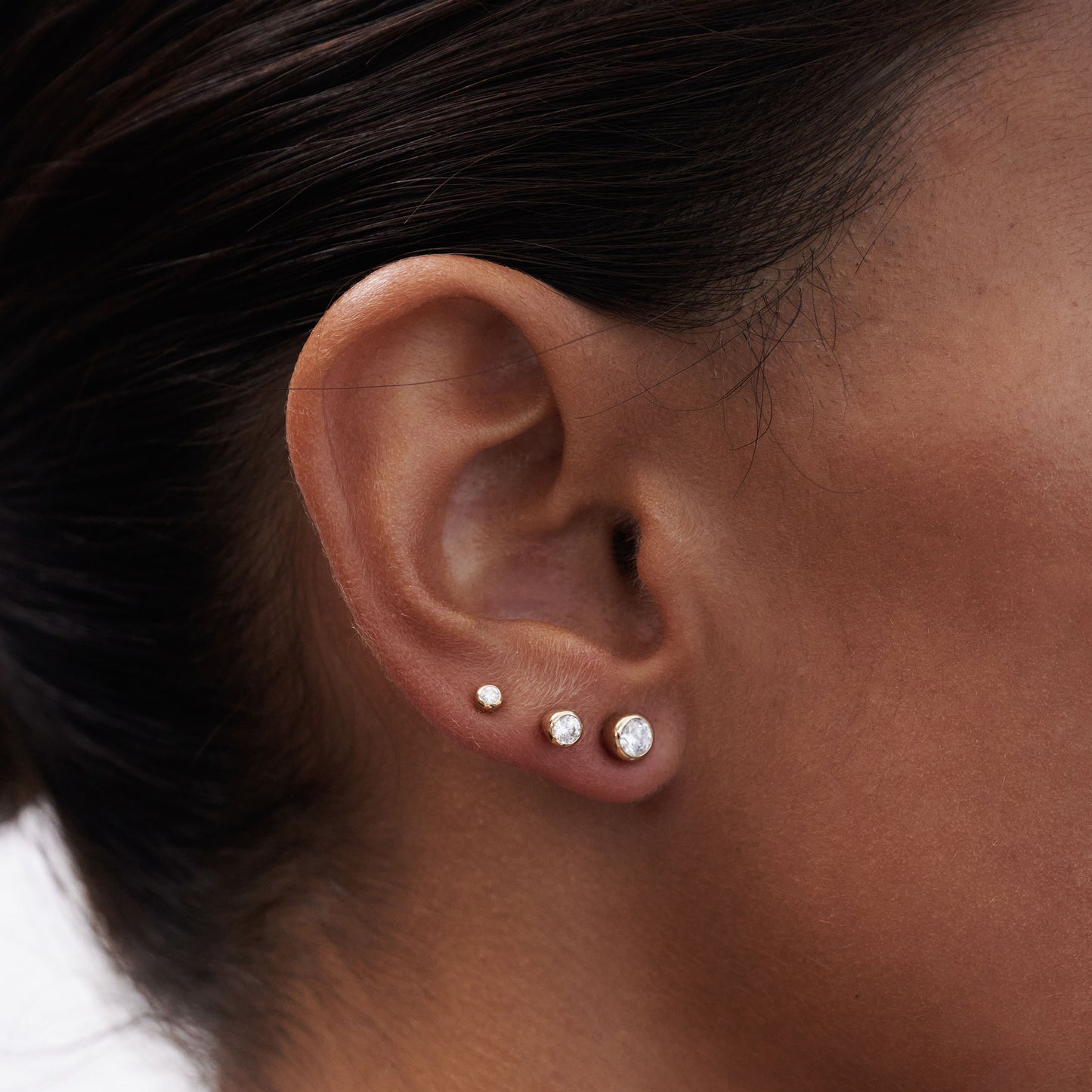 Close-up of ear featuring three diamond studs in varying sizes on the lobe, showcasing elegant luxury jewellery styling.