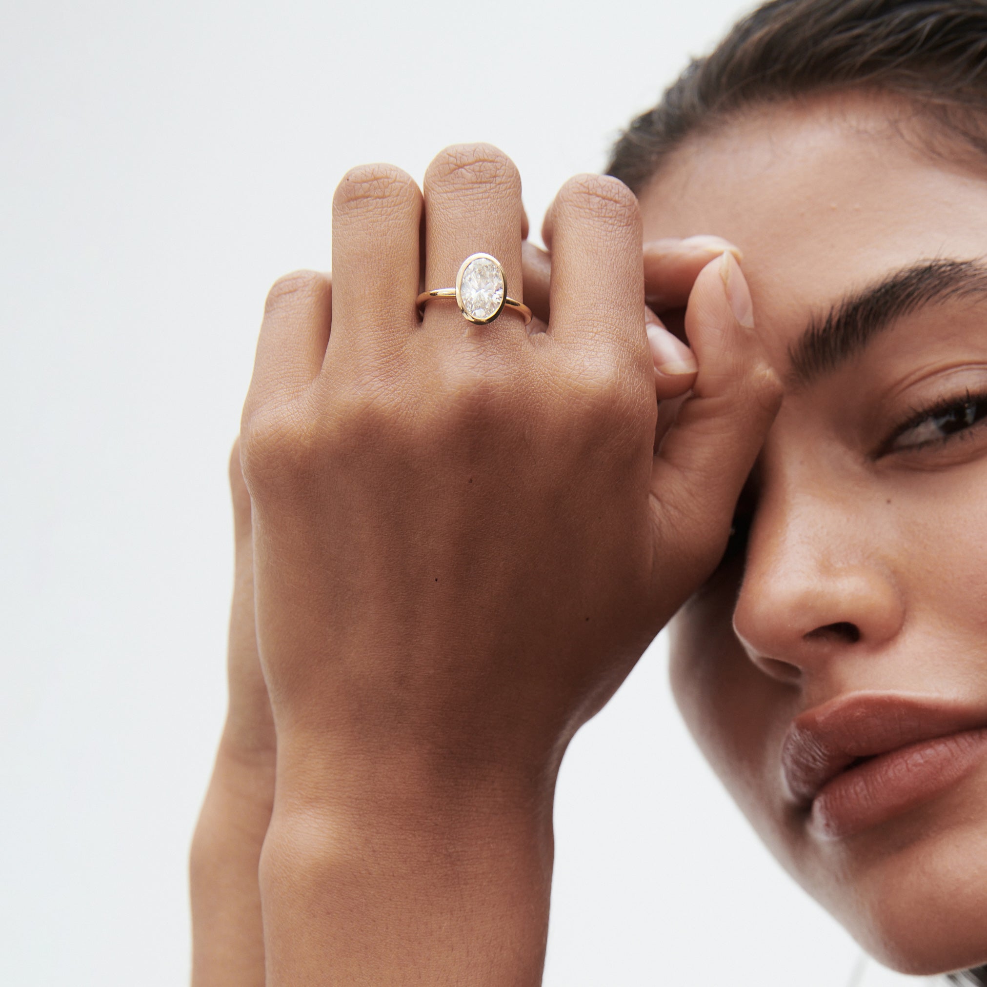 Woman displaying an elegant oval-cut diamond ring on her hand. Her face is partially visible, showcasing a sophisticated expression.