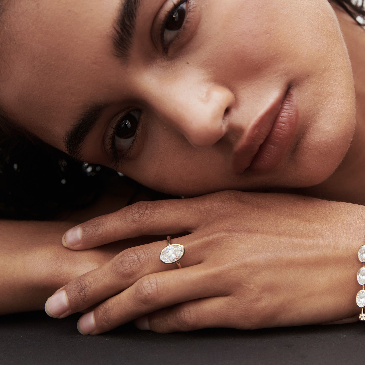 Woman resting her head on hands, showcasing an oval diamond ring and bracelet. Luxurious jewellery fashion. Close-up detail.