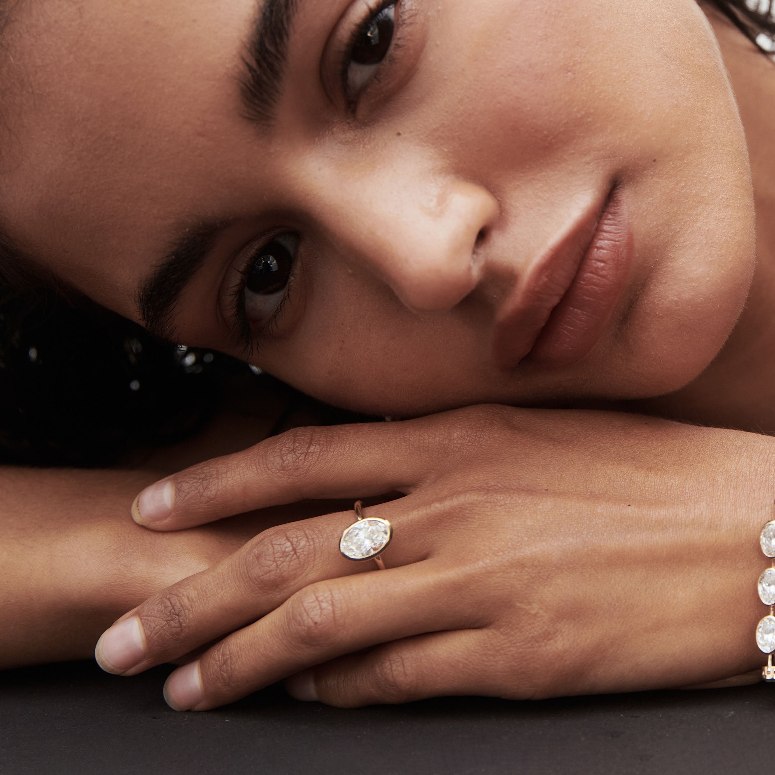 Woman resting her head on hands, showcasing an oval diamond ring and bracelet. Luxurious jewellery fashion. Close-up detail.