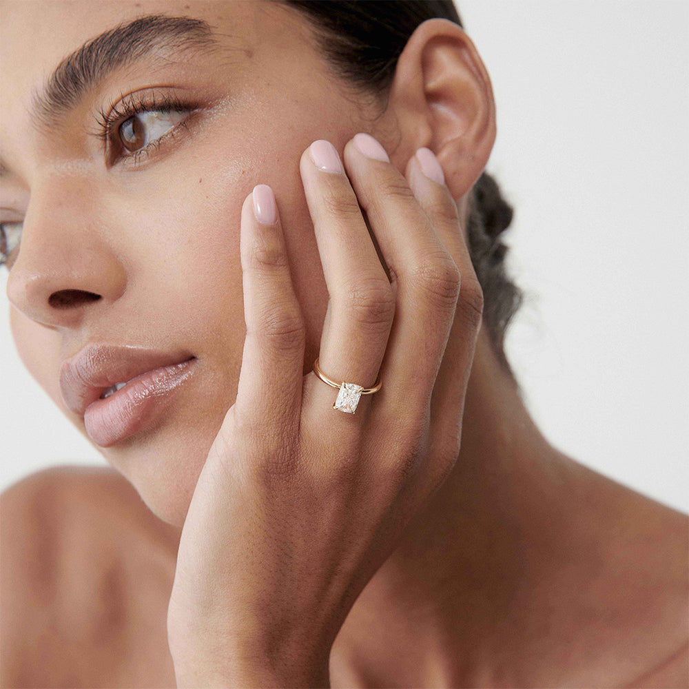 Close-up of a woman showcasing a solitaire diamond ring on her finger, with a soft, neutral background.