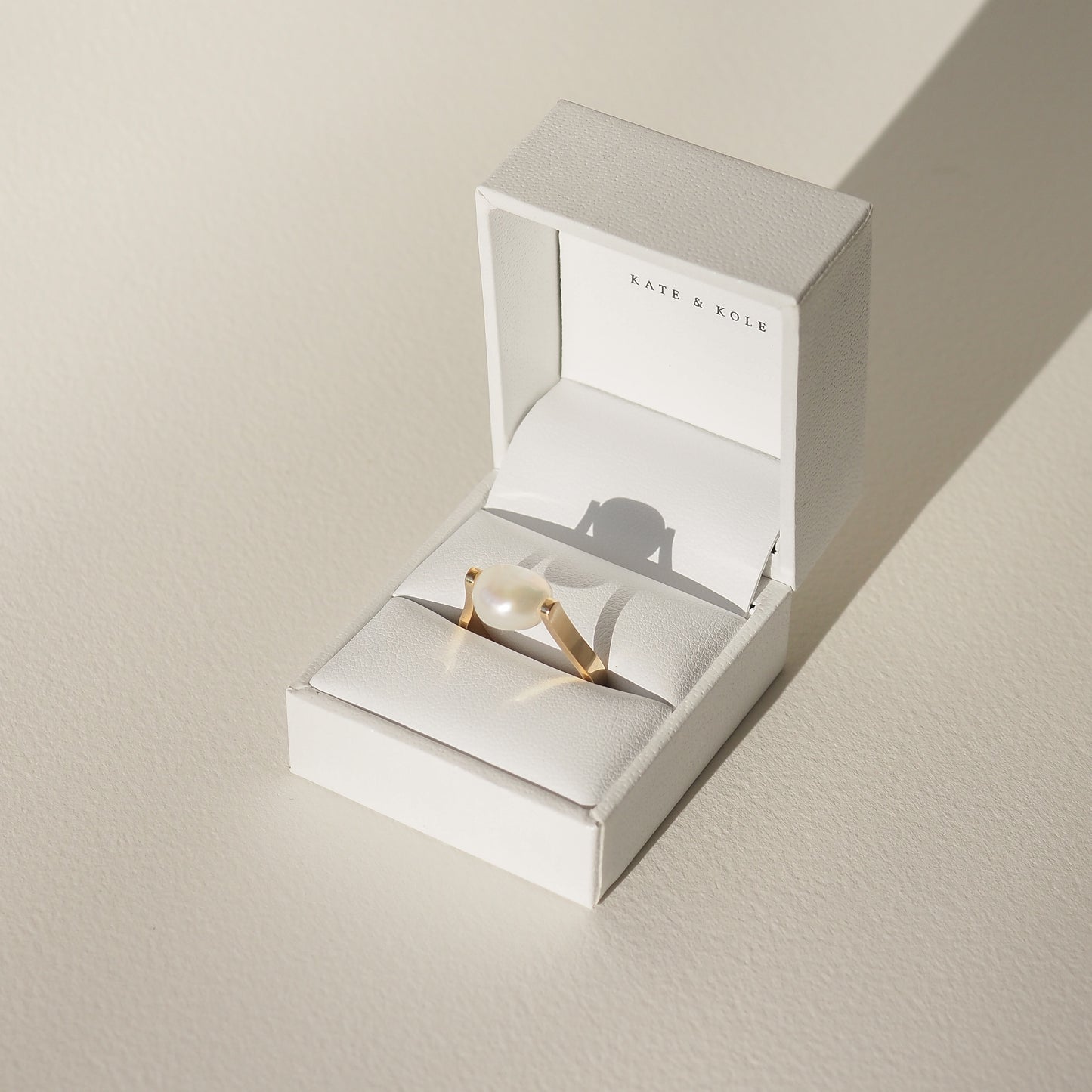 Elegant pearl ring in a white jewellery box, featuring delicate gold band, displayed in soft light. Perfect example of luxurious accessories.