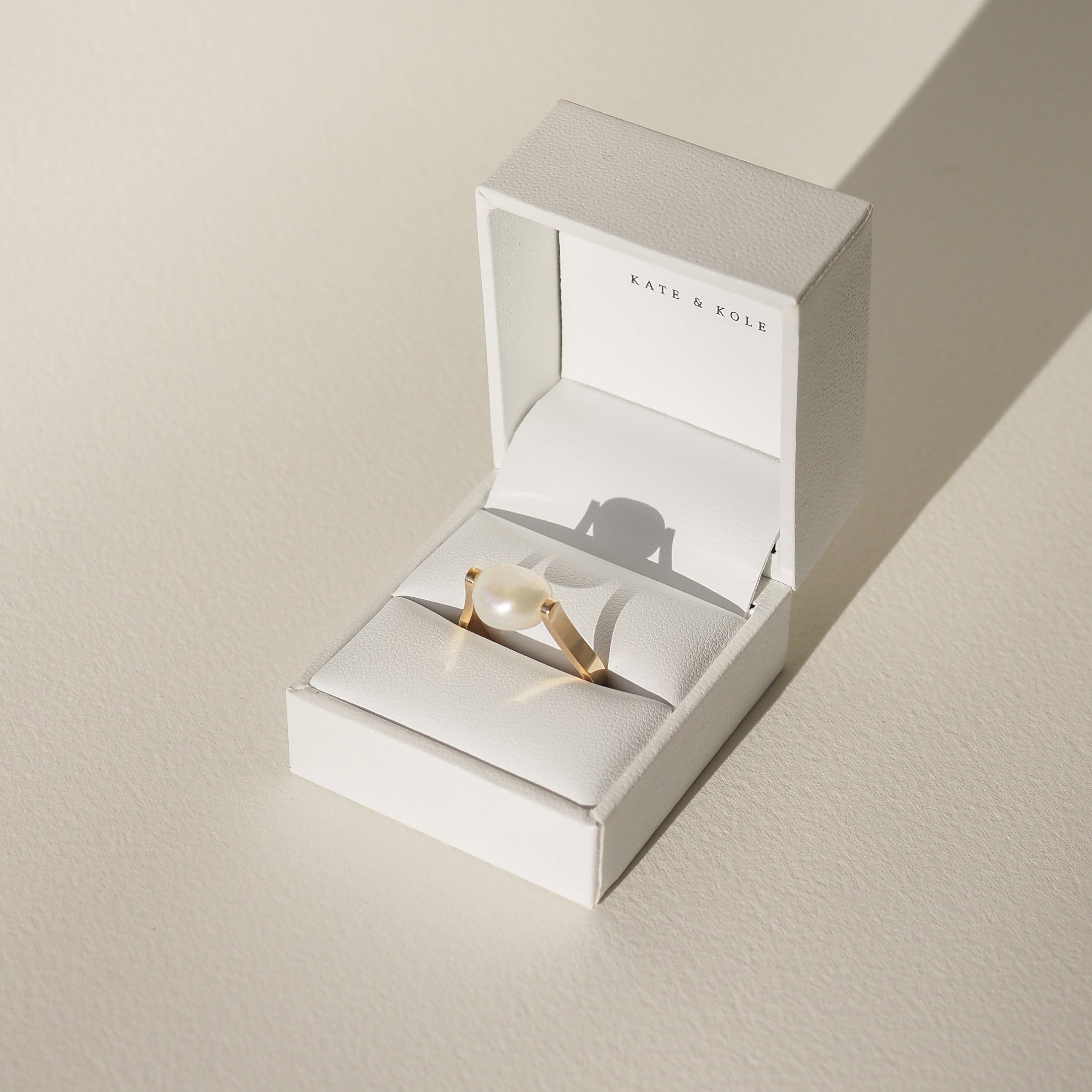 Elegant pearl ring in a white jewellery box, featuring delicate gold band, displayed in soft light. Perfect example of luxurious accessories.