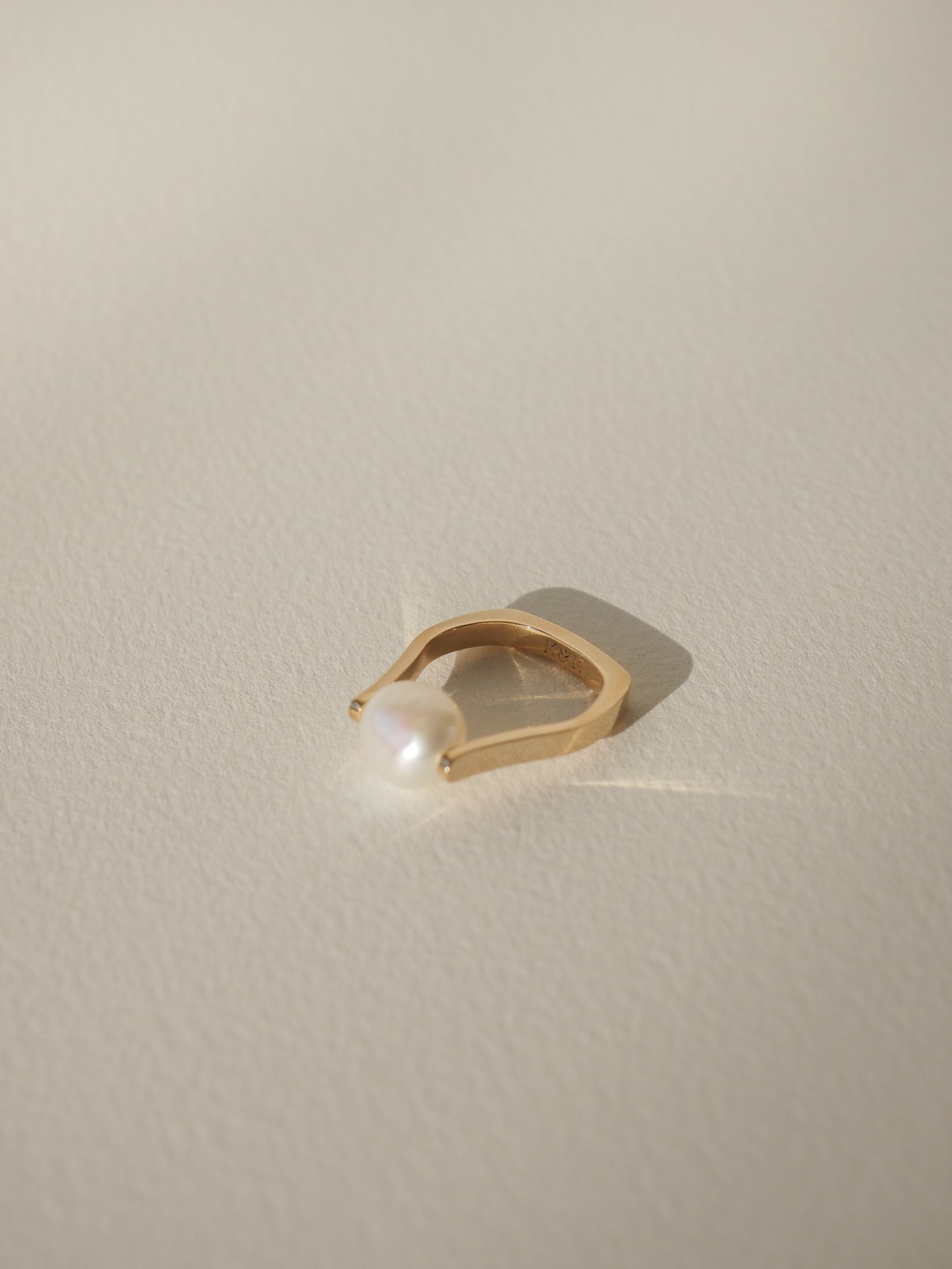 Elegant gold ring with a large white pearl, casting a gentle shadow on a soft, cream surface. High-end luxury jewellery.