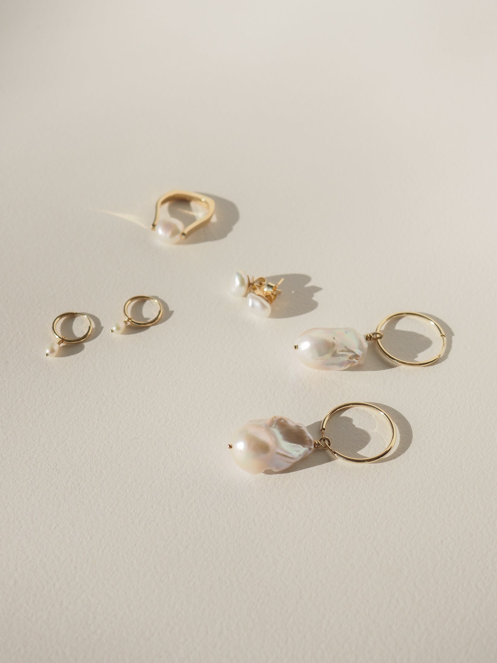 Minimalist jewellery set featuring gold rings and earrings with large baroque pearls, elegantly displayed on a soft beige surface.