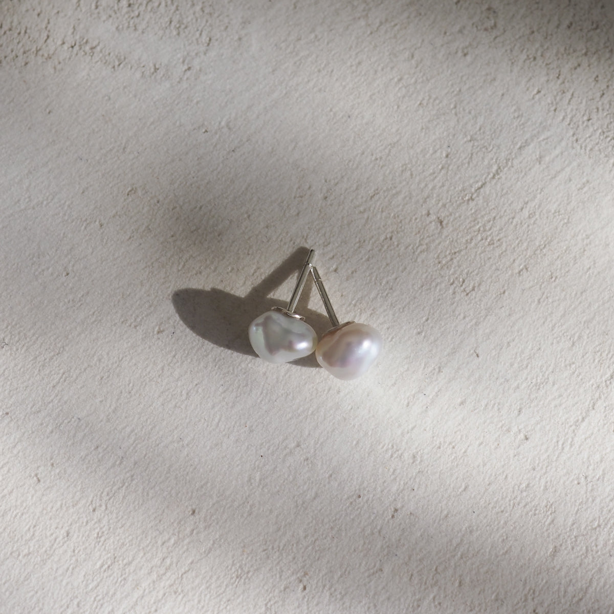 Baroque pearl earrings on a textured, light background, casting soft shadows. Perfect for luxury jewellery lovers.