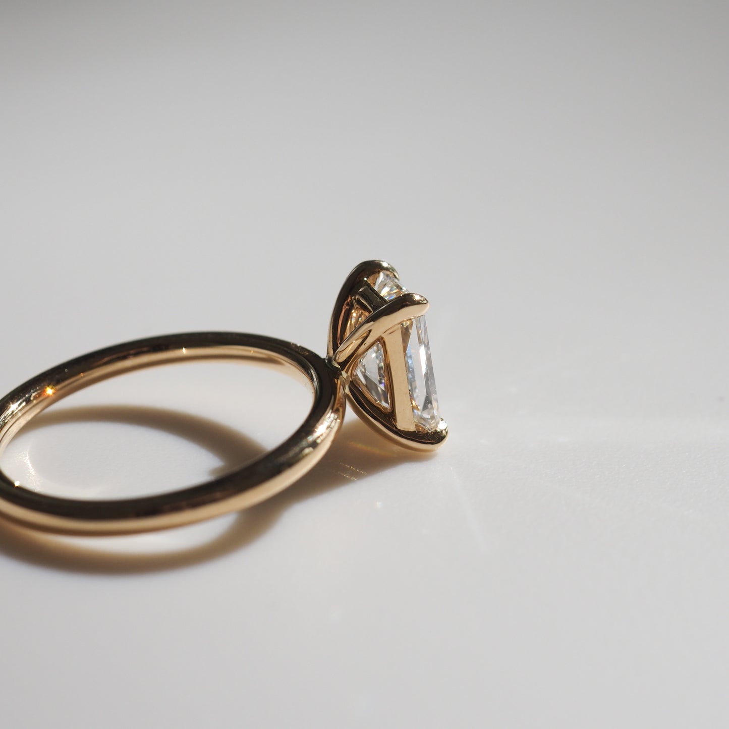 Gold ring with a large, clear diamond in a unique setting on a reflective surface. Elegant luxury jewellery with minimalist design.