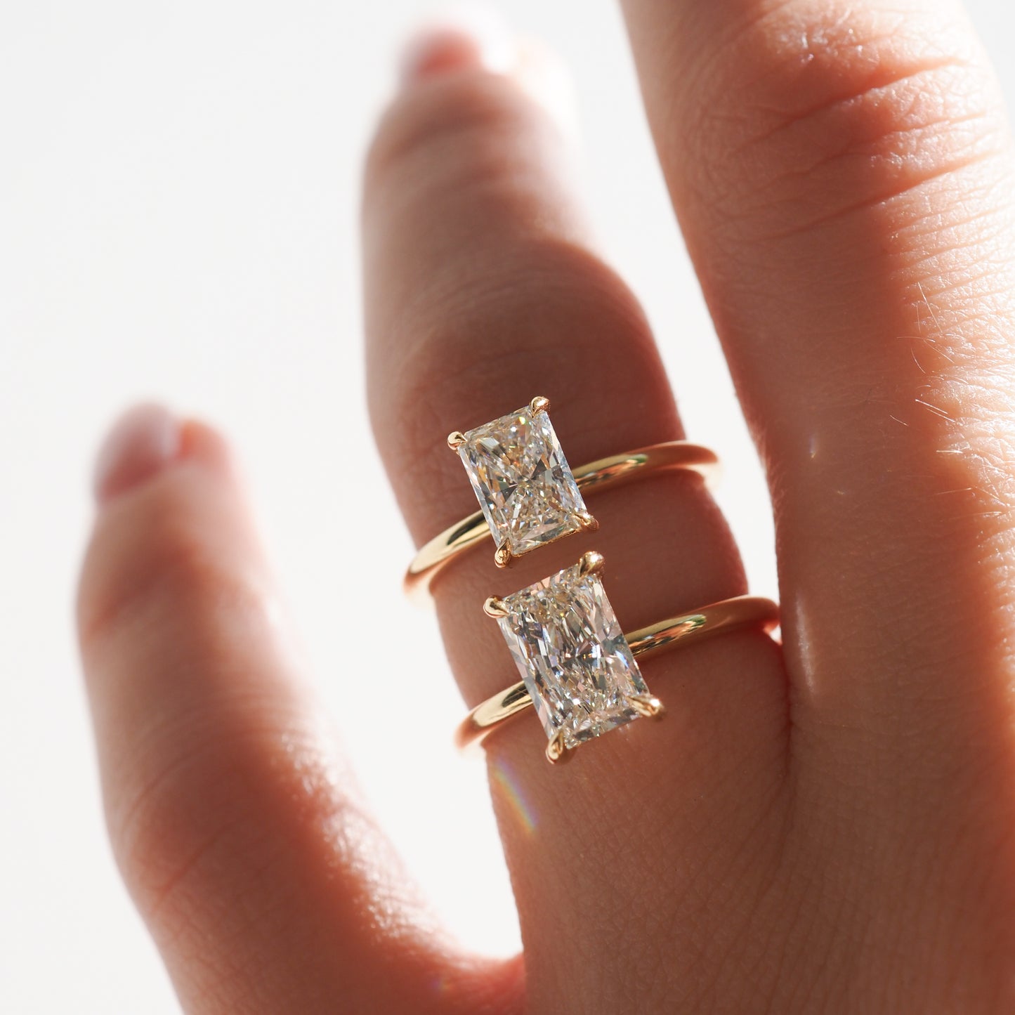 Two gold rings with radiant-cut diamonds displayed on a hand, showcasing luxury jewellery design in natural light.