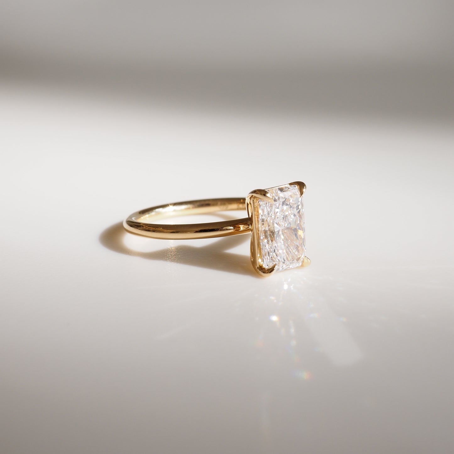 Gold ring with a radiant-cut diamond on a plain band. The diamond catches light, creating sparkles. Luxurious and elegant jewellery piece.