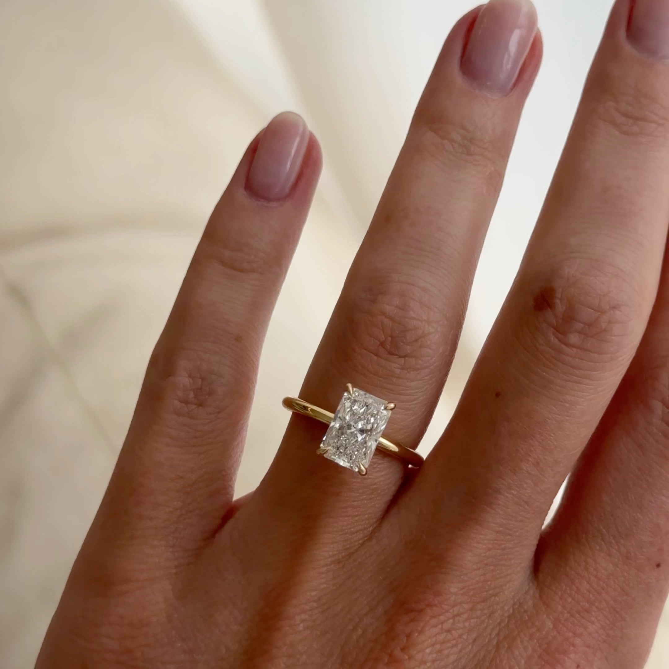 Close-up of a hand wearing a gold ring with a radiant-cut diamond. The person's nails are neatly manicured, showcasing luxury jewellery style.
