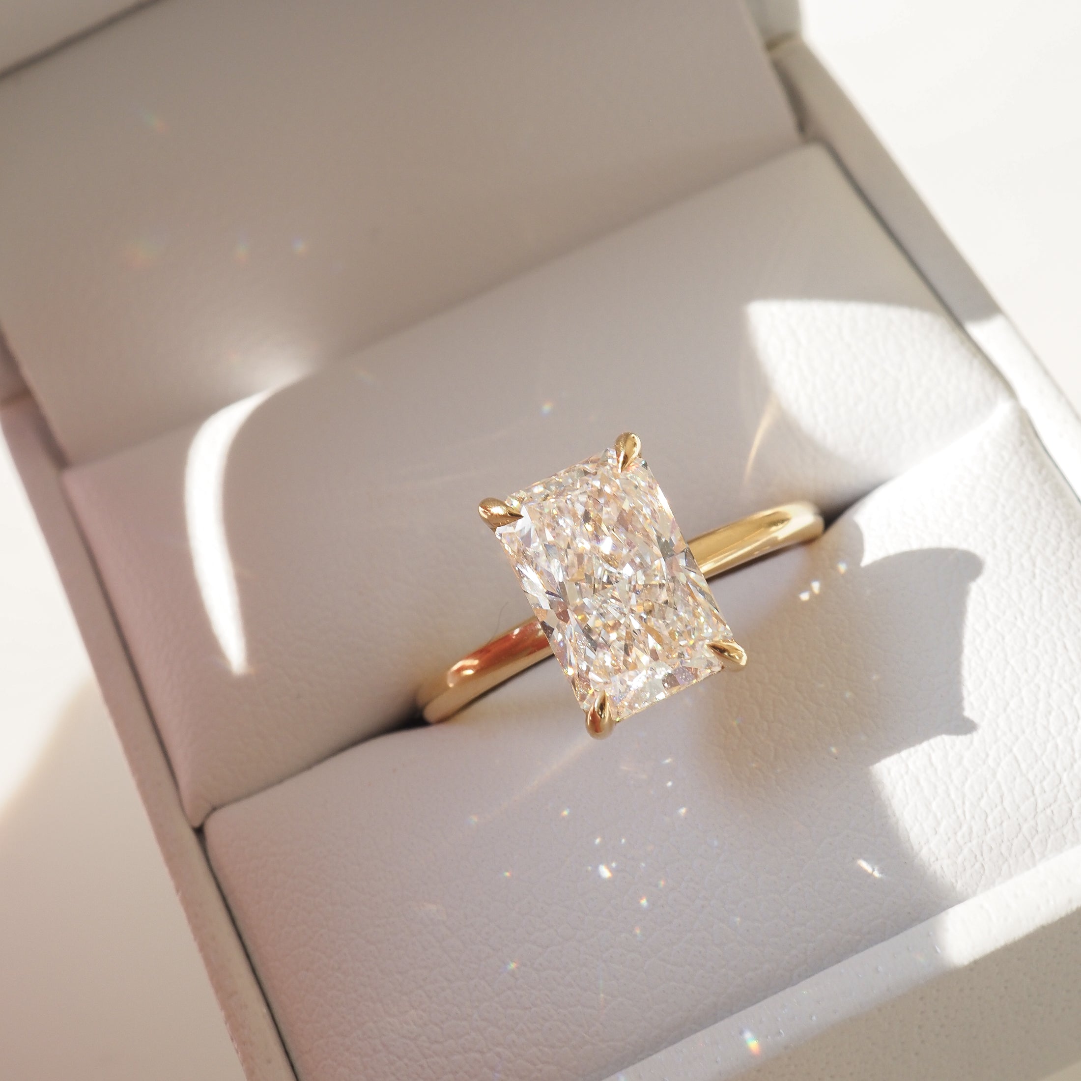 Luxury gold ring with radiant-cut diamond set in prongs, elegantly displayed in a white ring box. Sparkling and sophisticated jewellery design.
