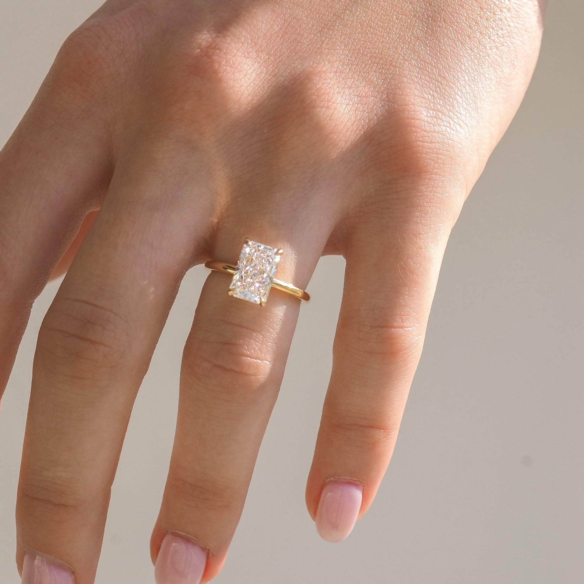 Close-up of hand wearing gold ring with large, rectangular-cut diamond. Luxury jewellery piece highlighting elegant simplicity.