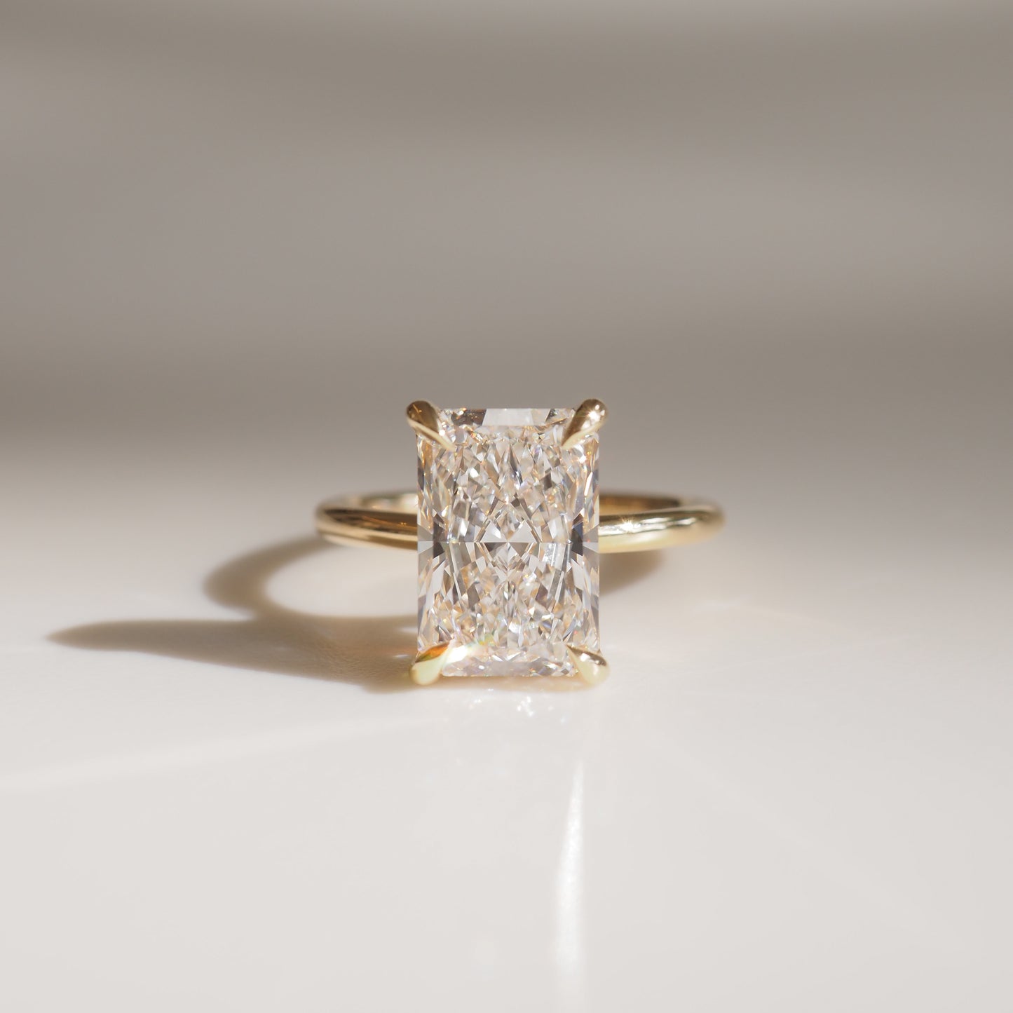 Radiant-cut diamond solitaire ring with a gold band, reflecting light on a soft surface. Luxury jewellery with simple elegance.