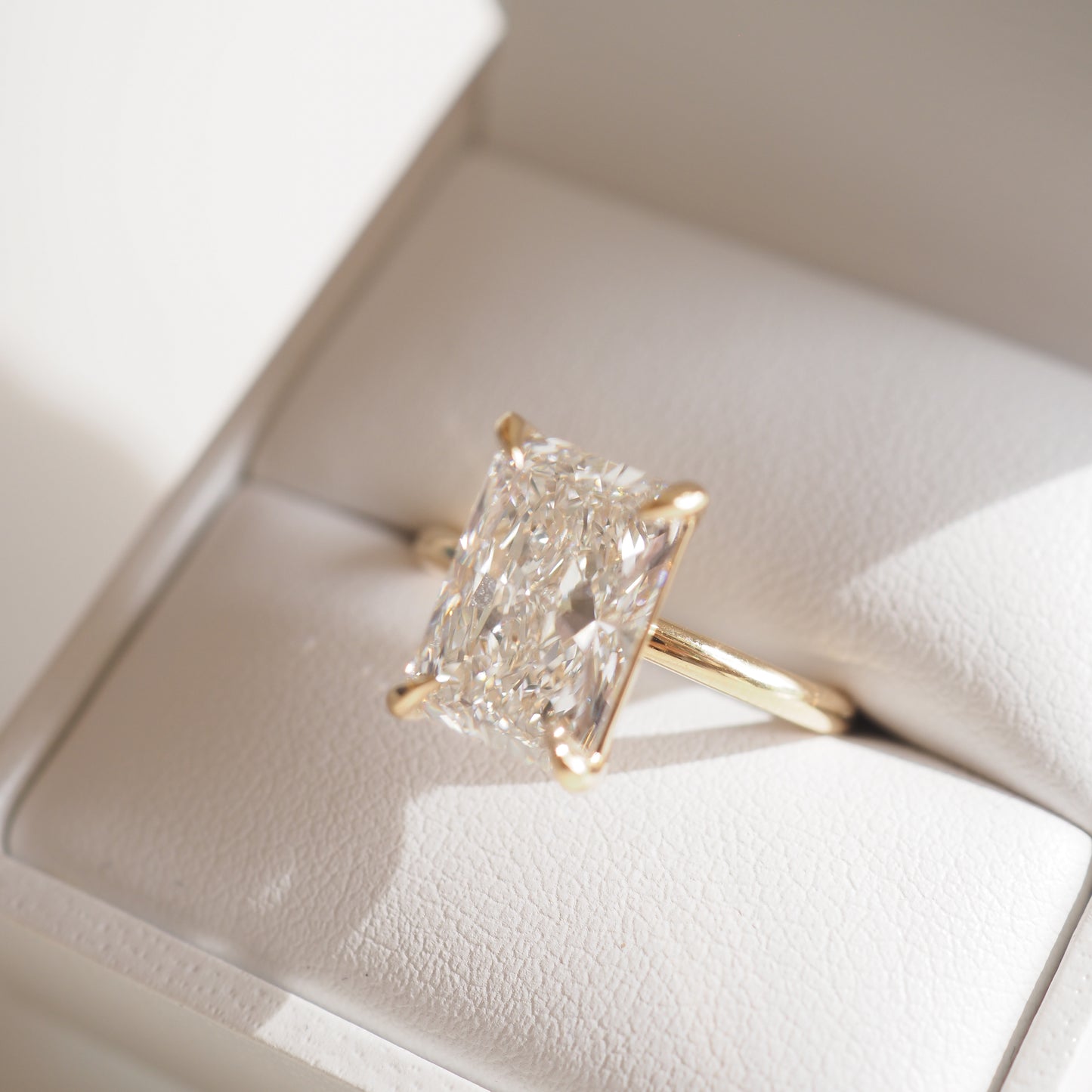 Gold ring with a large rectangular diamond in a white jewellery box, catching natural light; elegant luxury jewellery.