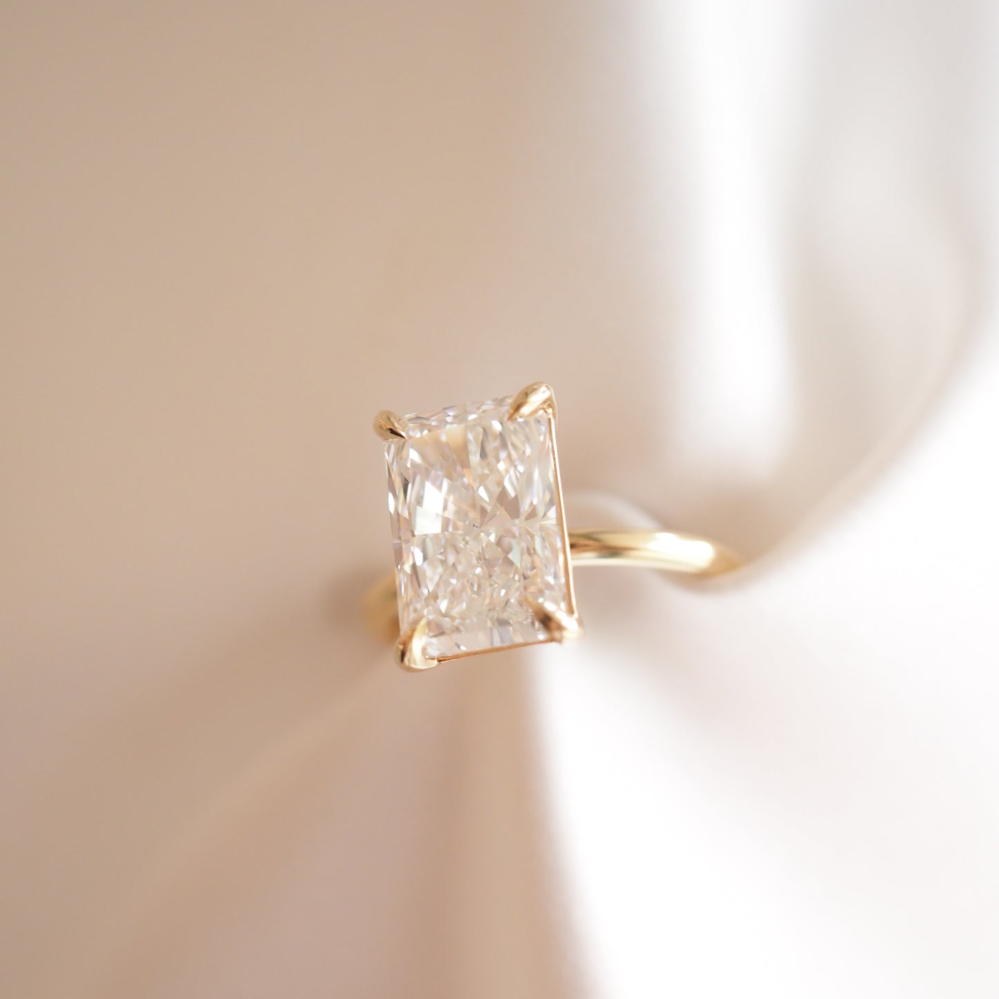 Rectangular diamond ring set in gold, placed on a soft white fabric. Luxurious jewellery and elegant design.