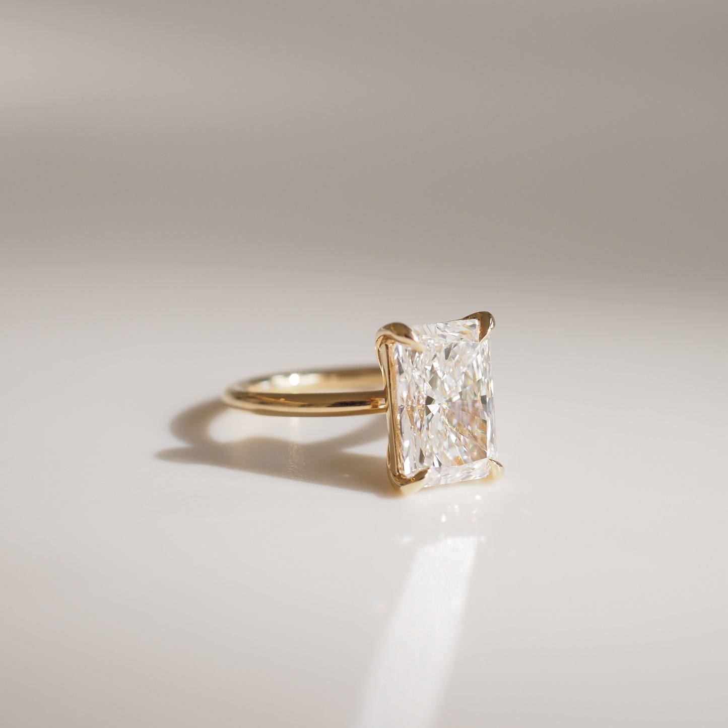 Elegant gold ring with a radiant rectangular diamond solitaire, showcased against a soft, neutral background, highlighting luxury jewellery.