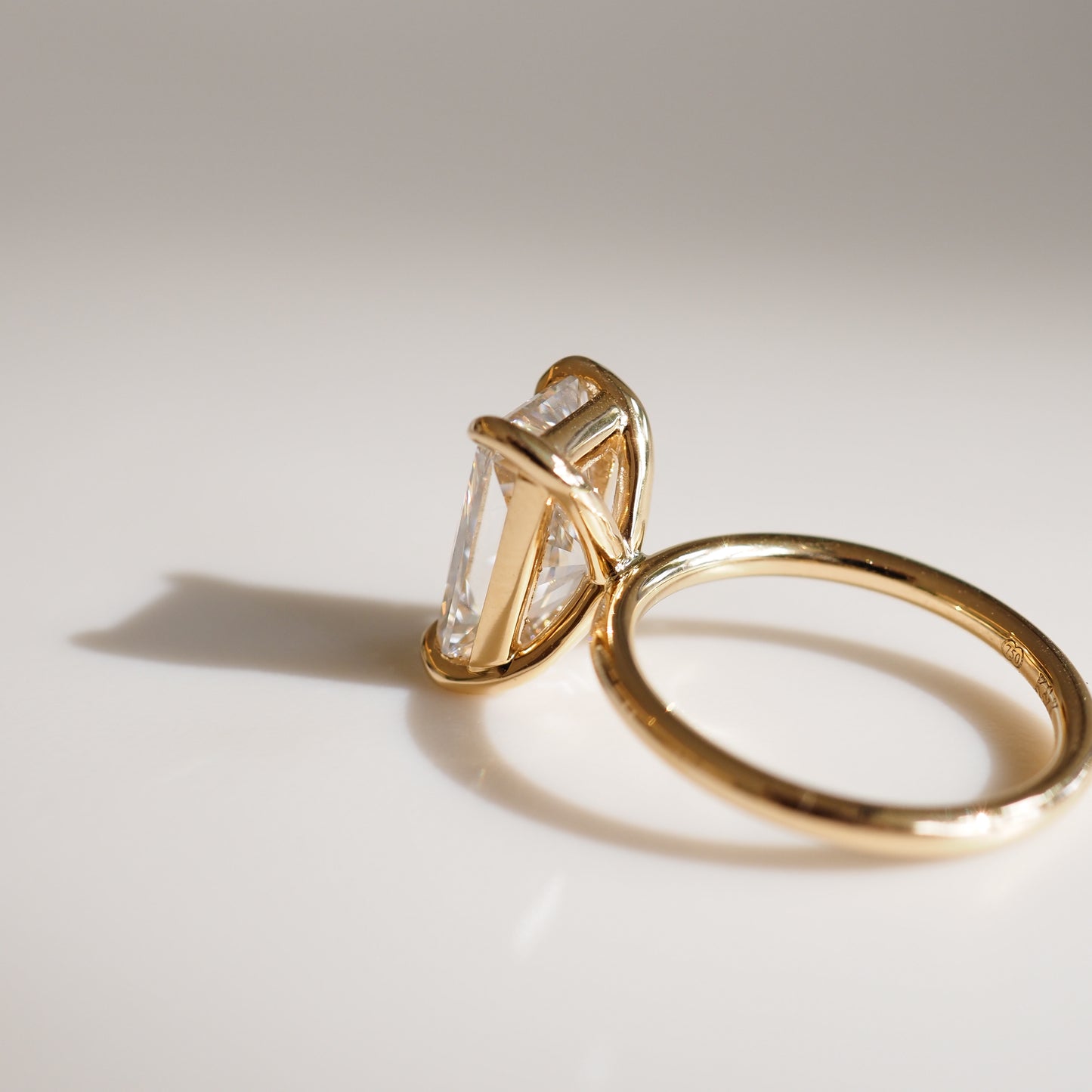 Elegant gold ring with a large diamond, elegantly displayed on a reflective surface, casting a soft shadow. Luxury jewellery.