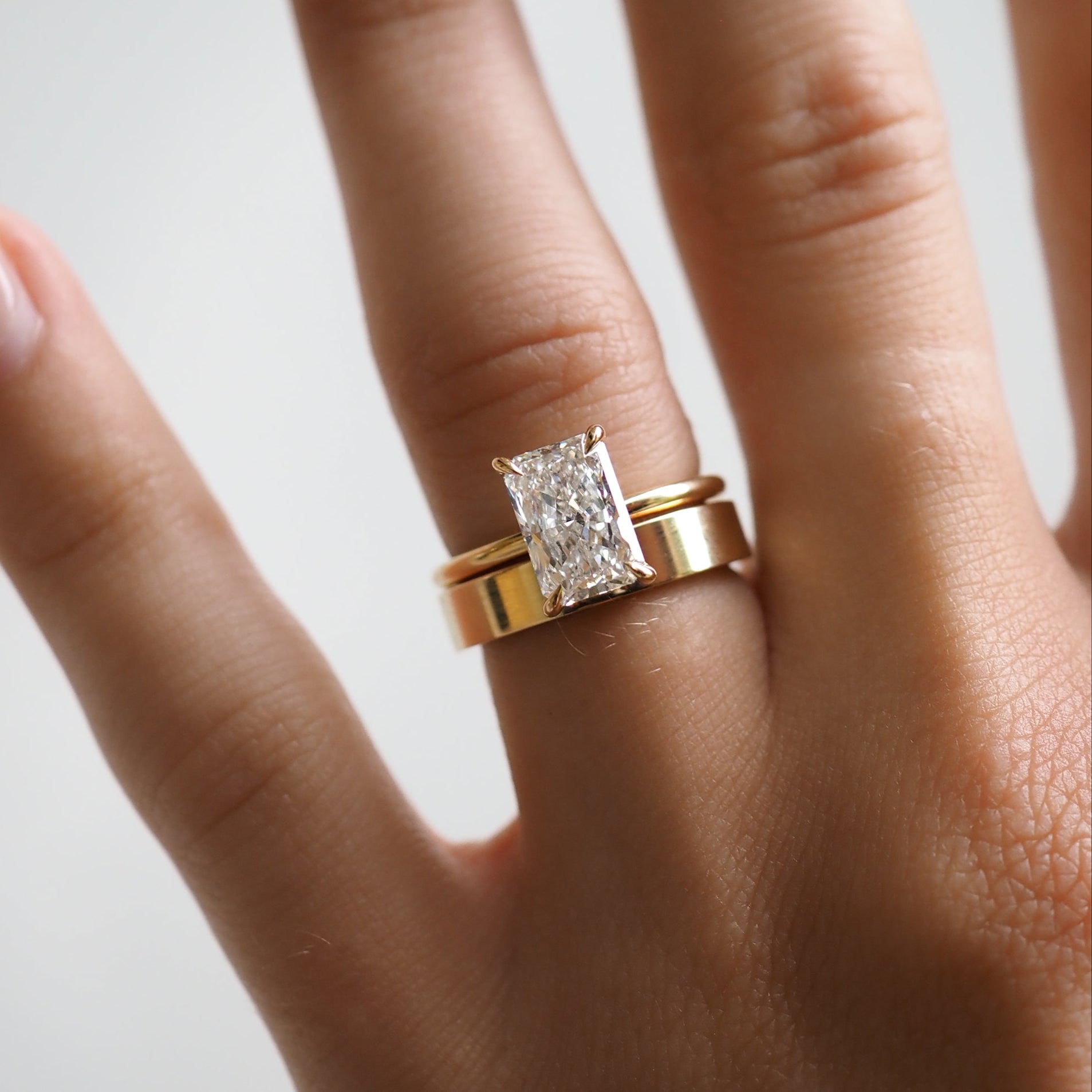 Hand wearing a gold band with a large rectangular diamond ring, showcasing luxury jewellery craftsmanship.