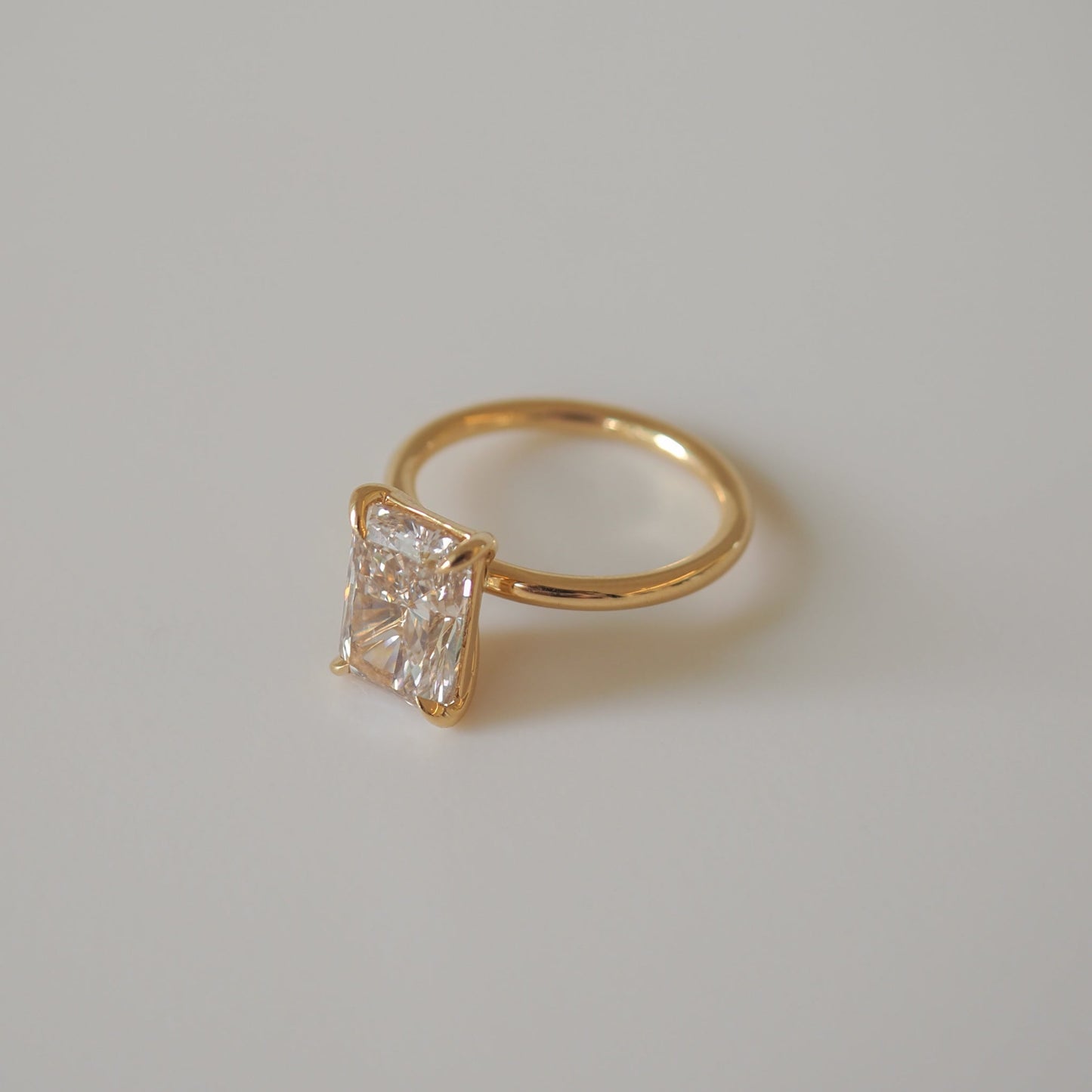 Gold ring with a large, rectangular-cut diamond set in a minimalist design, placed on a light grey background.