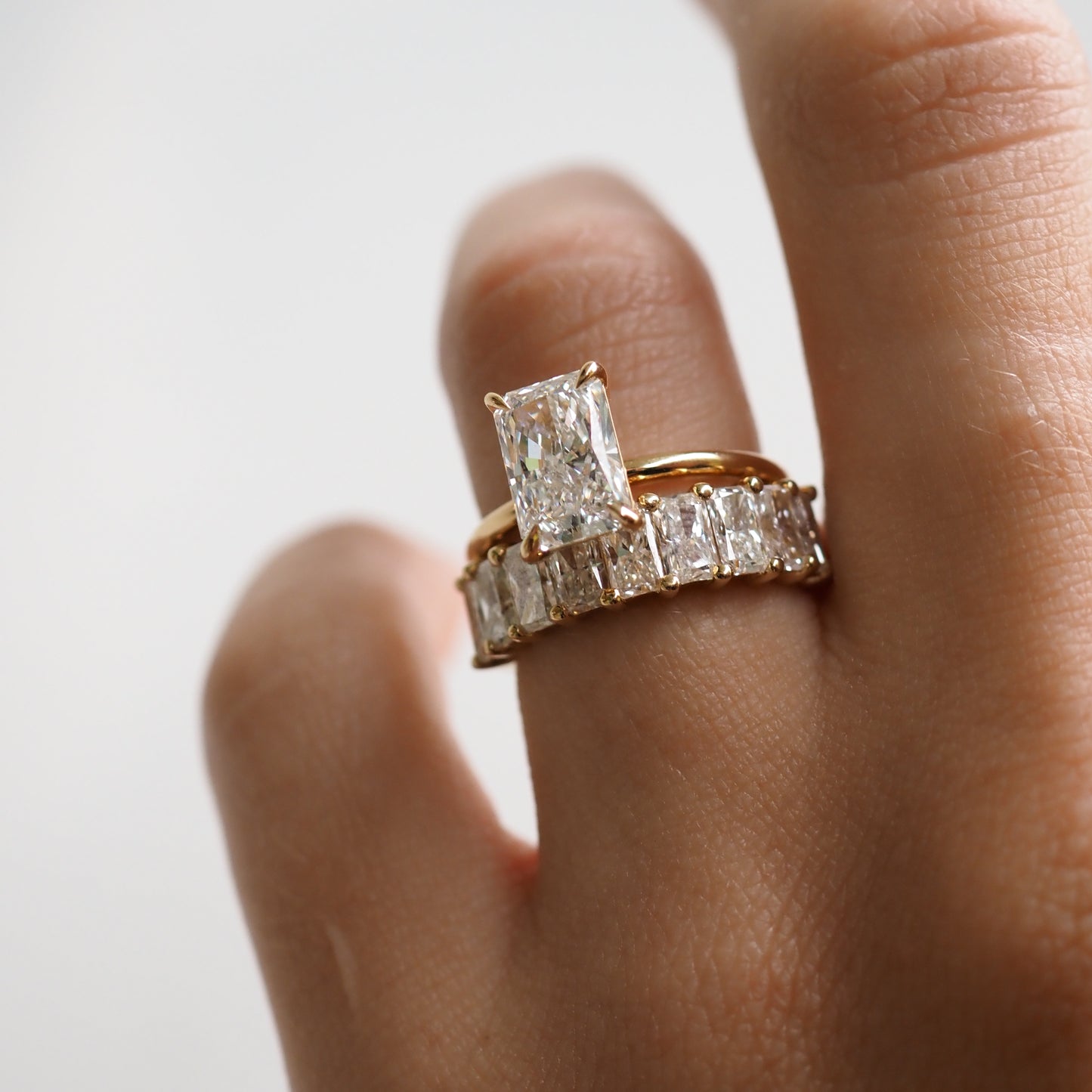 Elegant hand adorned with a gold band featuring a large rectangular diamond and a matching eternity ring, exemplifying luxury jewellery design.