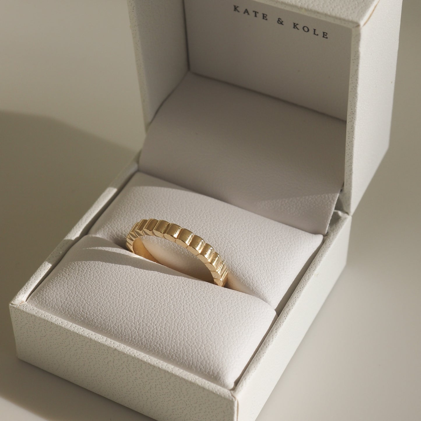 Gold ring with a ribbed design in a white jewellery box by Kate & Kole, reflecting luxury elegance.
