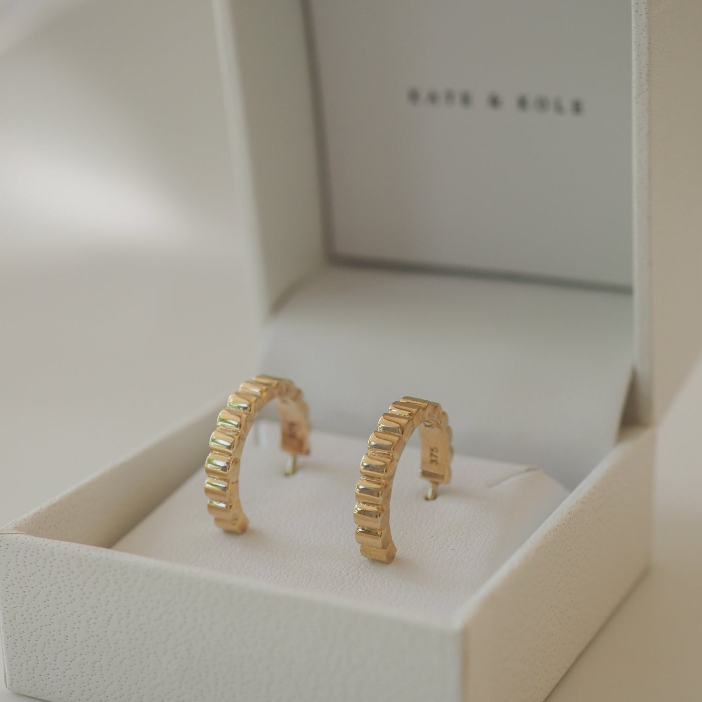 Gold hoop earrings with rectangular design, displayed in an elegant white jewellery box.