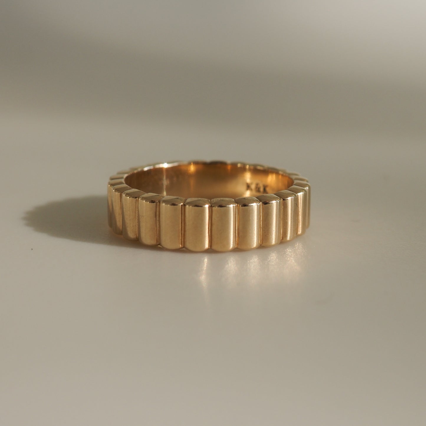 Elegant gold ring with a ribbed design, reflecting light on a plain surface. Perfect for luxury jewellery lovers.