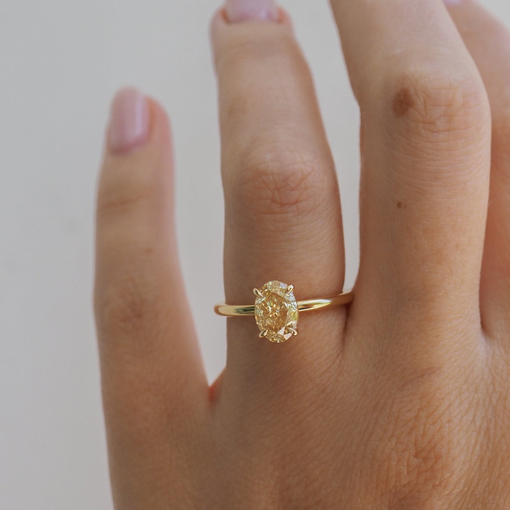 Hand wearing a gold ring with an oval yellow diamond, set in a minimalist band, showcasing elegance and luxury jewellery.