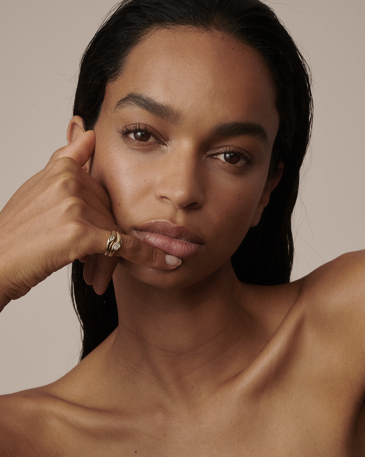 A close-up portrait of a woman with dark hair and warm skin tones, wearing a gold ring on her finger, set against a solid beige background.  [text overlay: 0.15ct left and 0.25ct right]