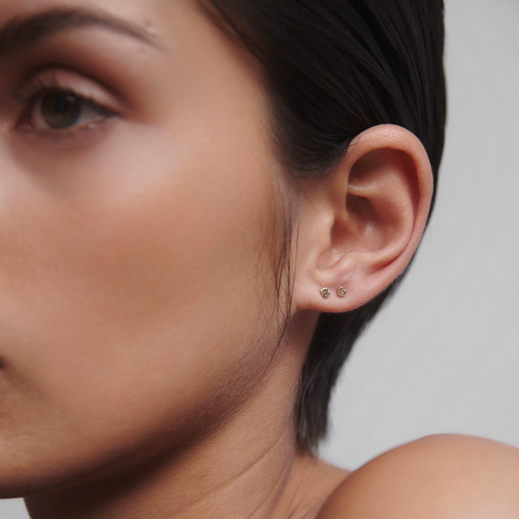 Close-up of a woman's ear showcasing two elegant gold stud earrings, highlighting minimalist luxury jewellery design.