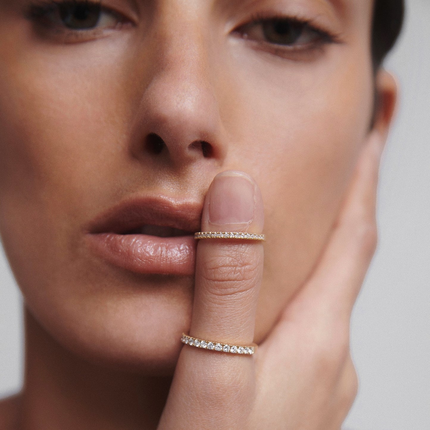 Woman with two diamond rings on finger, posing thoughtfully with hand on face. Luxury jewellery close-up.