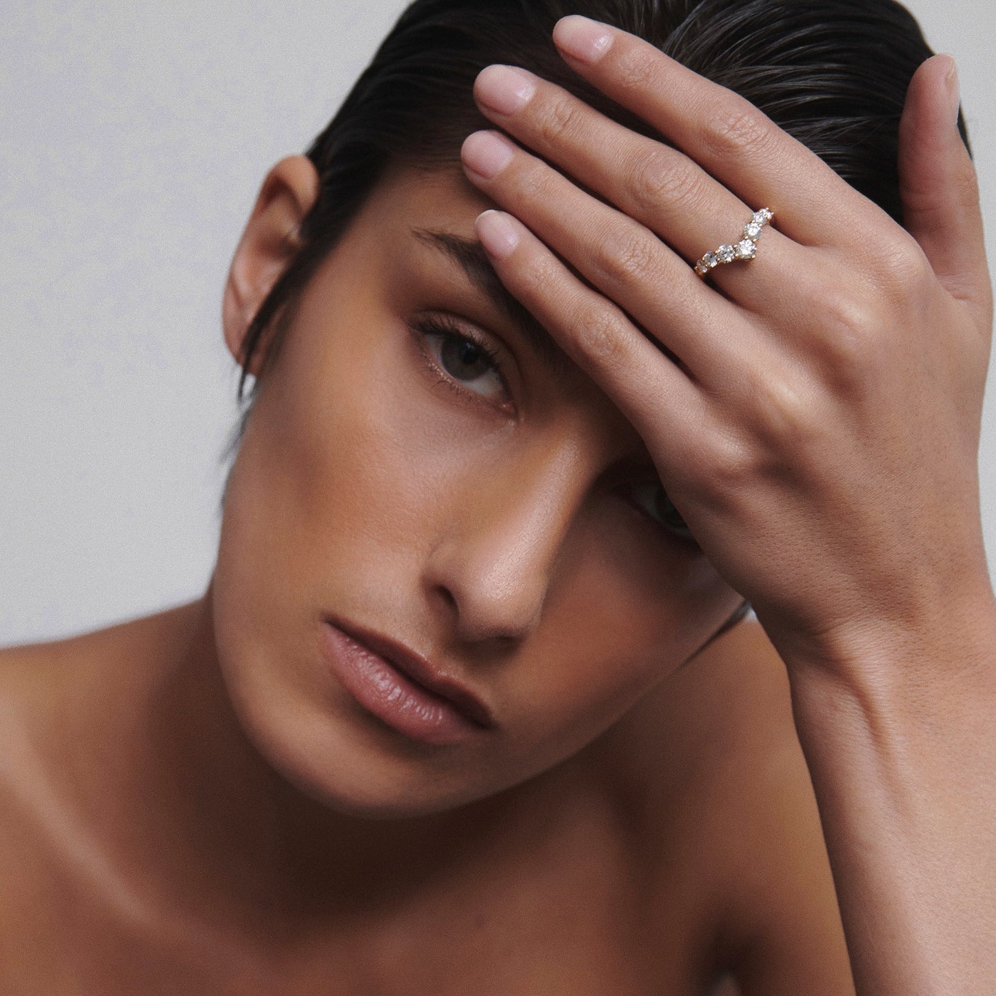 Woman with slicked-back hair wearing a diamond ring, resting her hand on her forehead. Luxury jewellery, elegance and style.