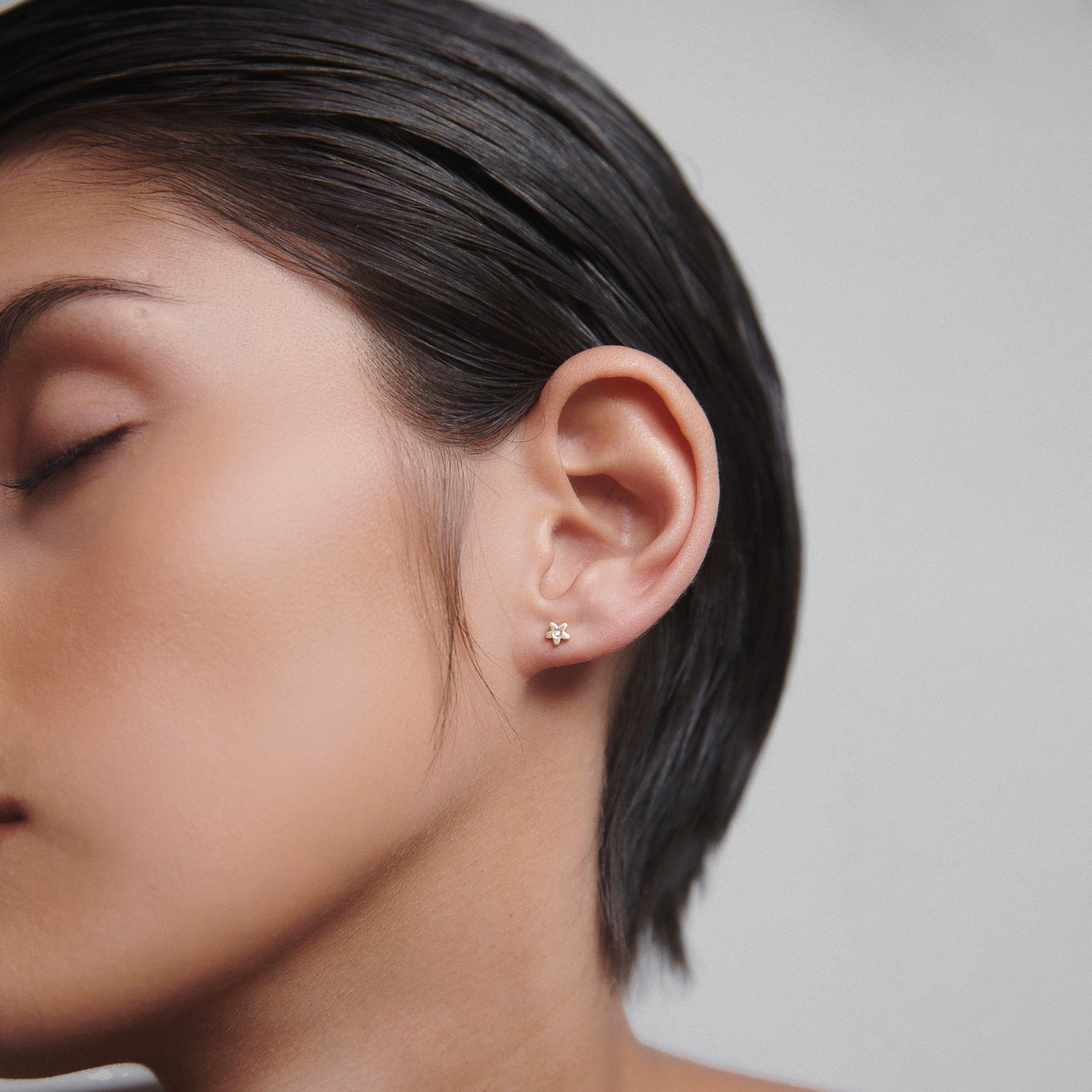 Close-up of a person wearing an elegant gold stud earring shaped like a flower, highlighting luxury jewellery against smooth skin.