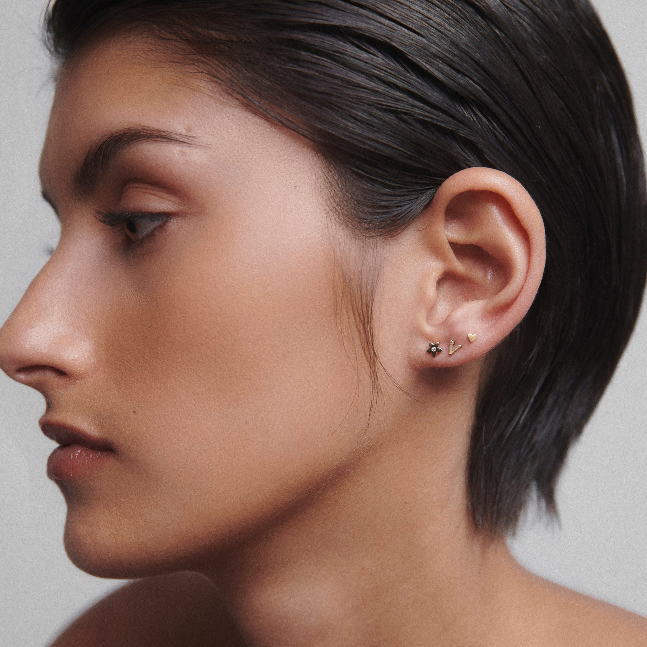 Profile of a woman with short hair wearing multiple gold and diamond earrings. Luxurious and elegant jewellery style.
