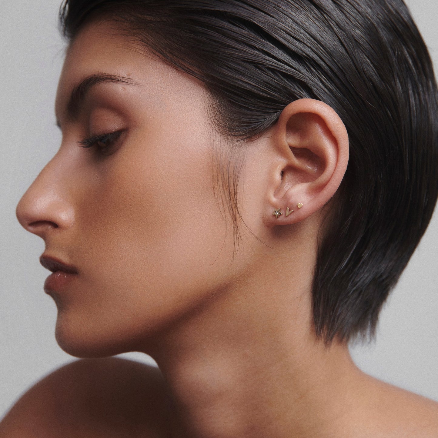 Profile of a person with sleek hair showcasing elegant gold ear climber earrings against a neutral background.